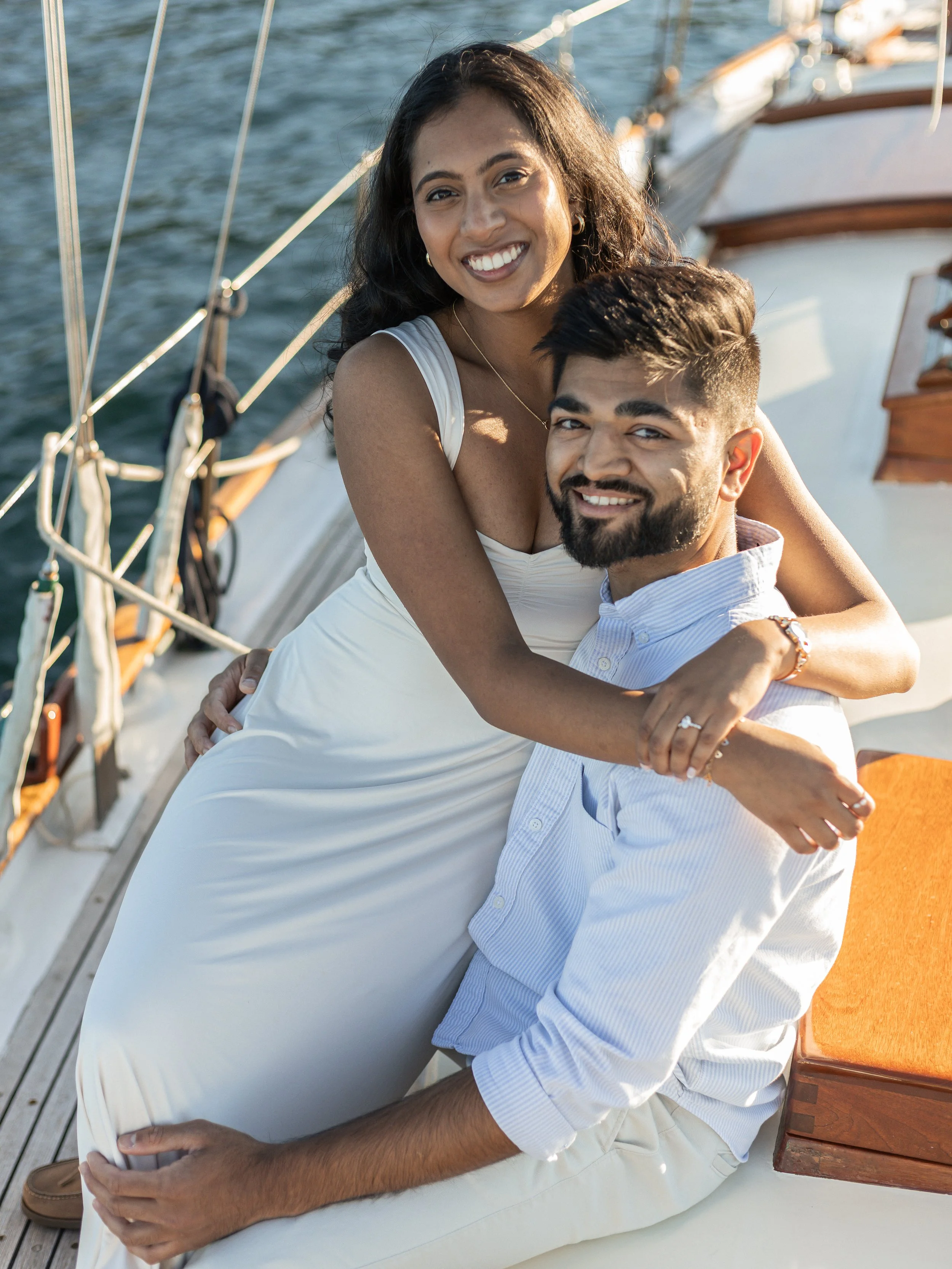 A couple sitting on a yacht, smiling and enjoying a sunny day by the water.