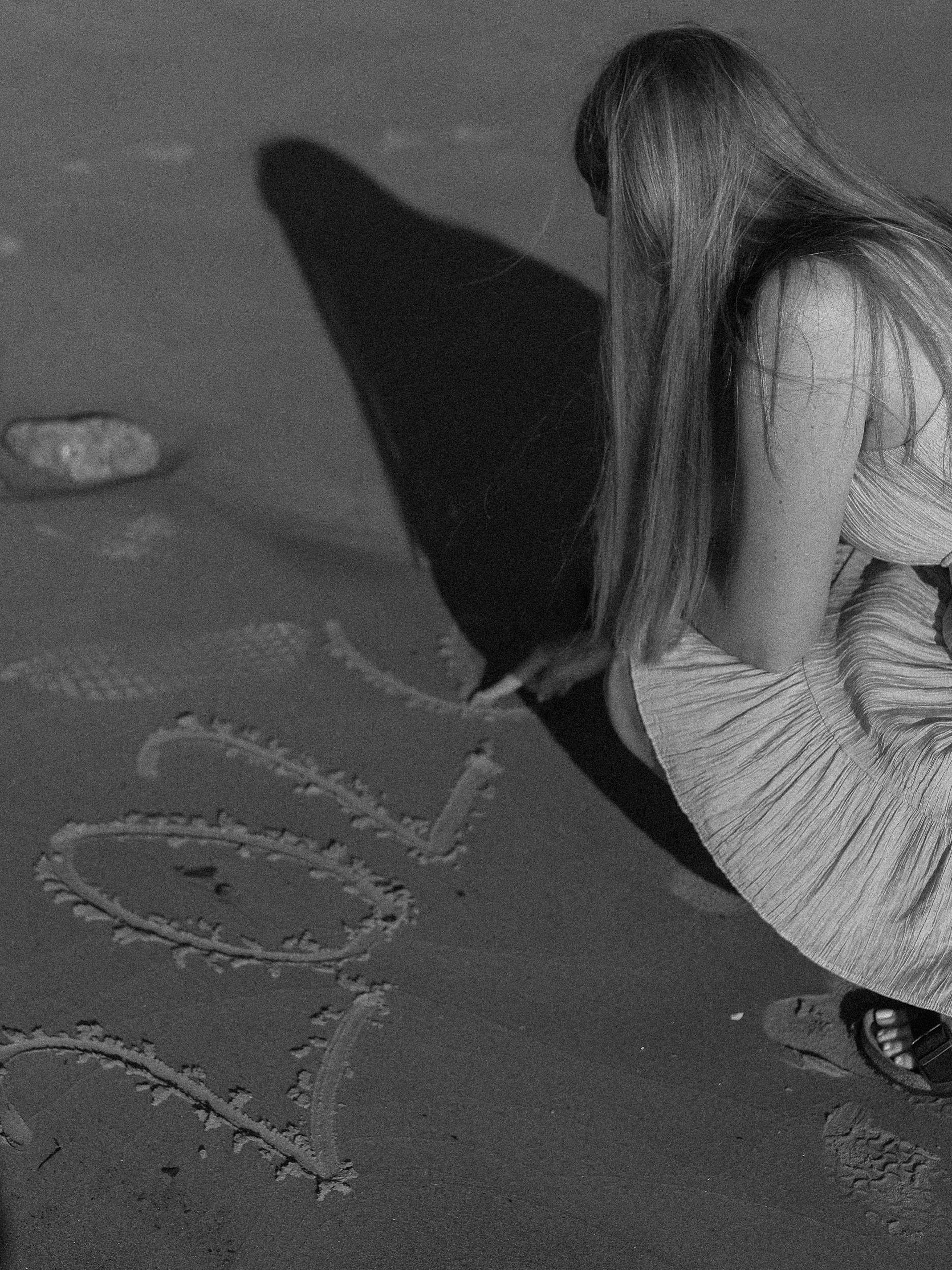 A girl with long hair writing 'love' in the sand on the beach