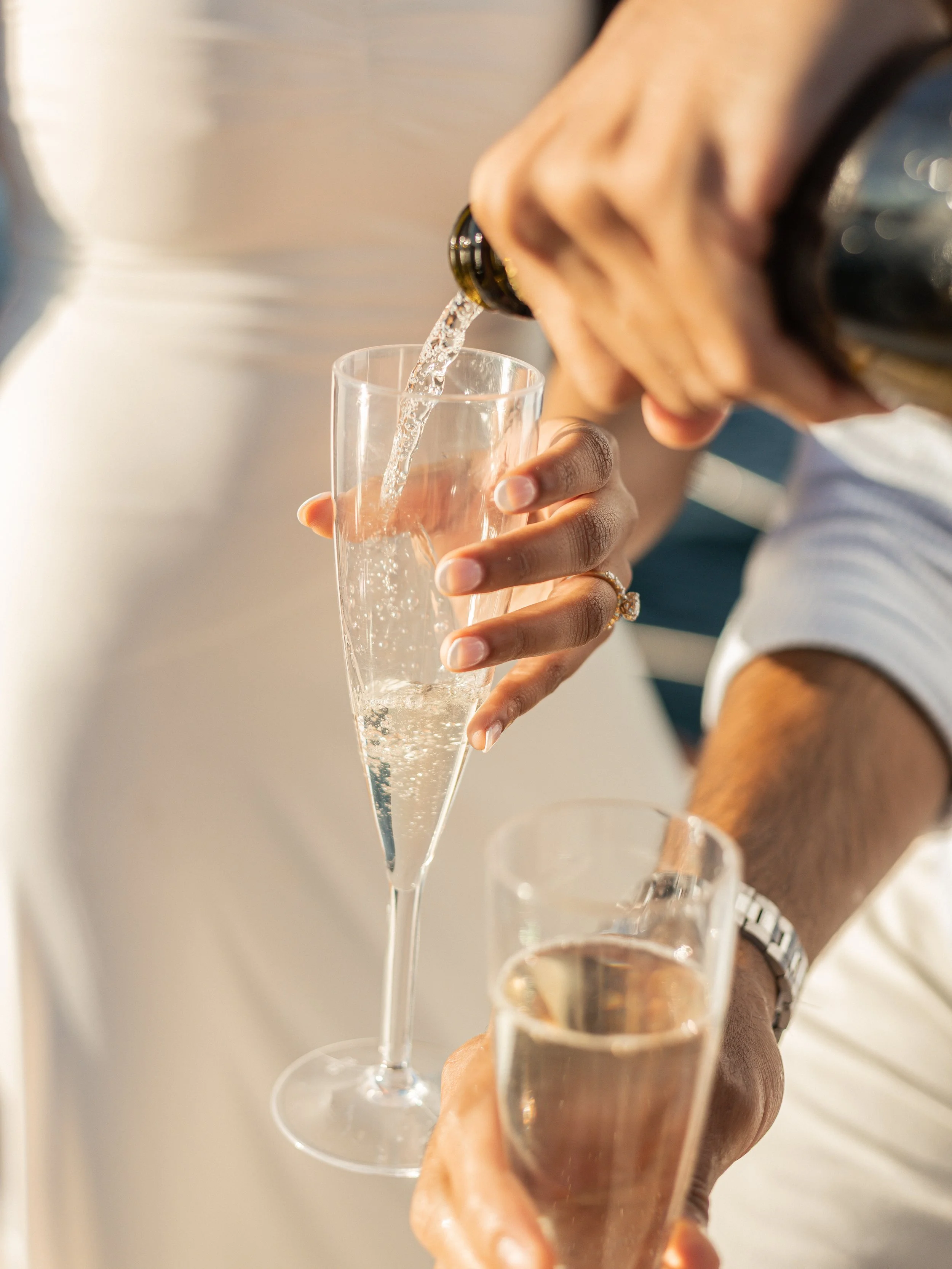 Person pouring champagne into a flute glass while holding another glass of champagne.