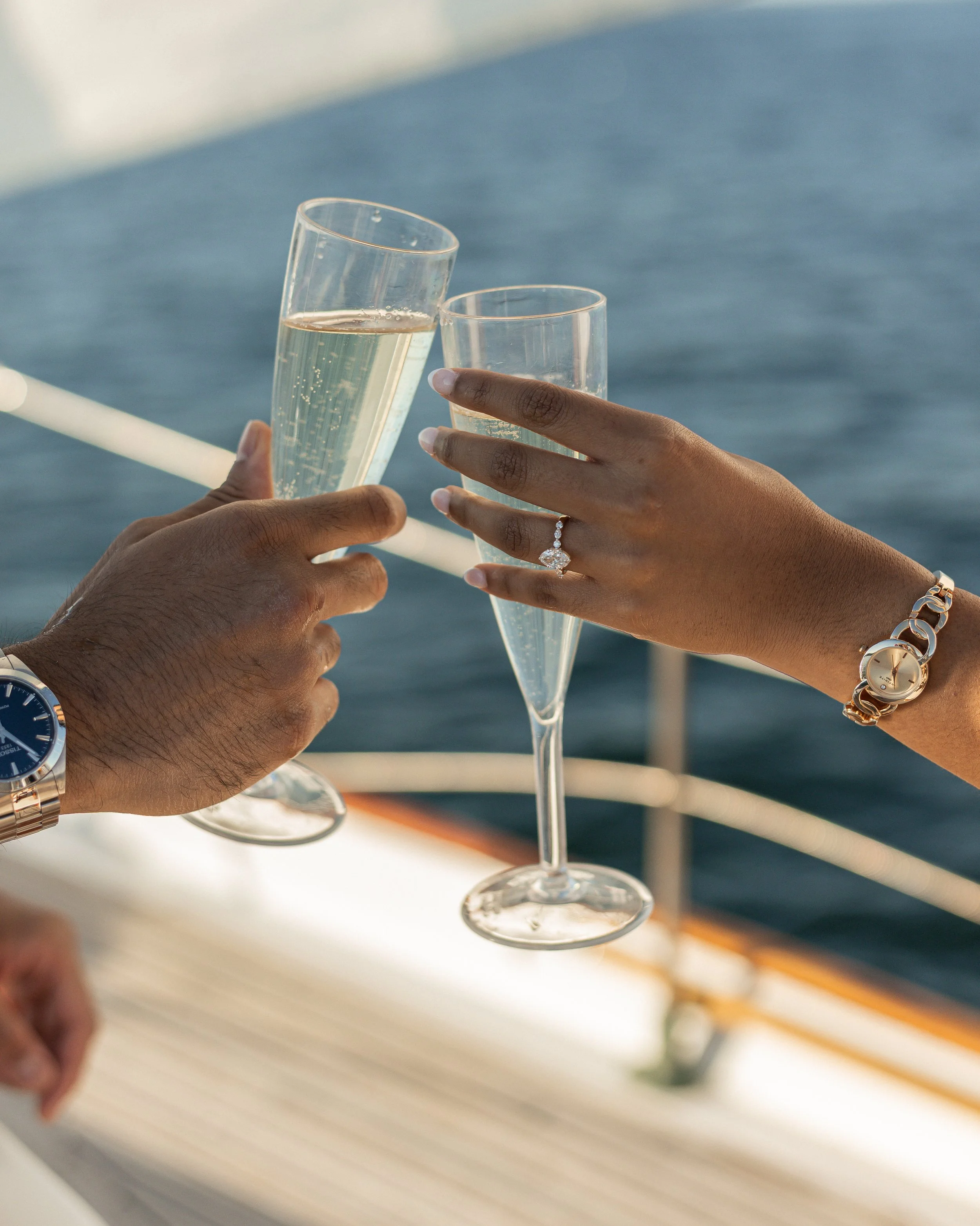 Two people clinking glasses of champagne on a boat with water in the background.