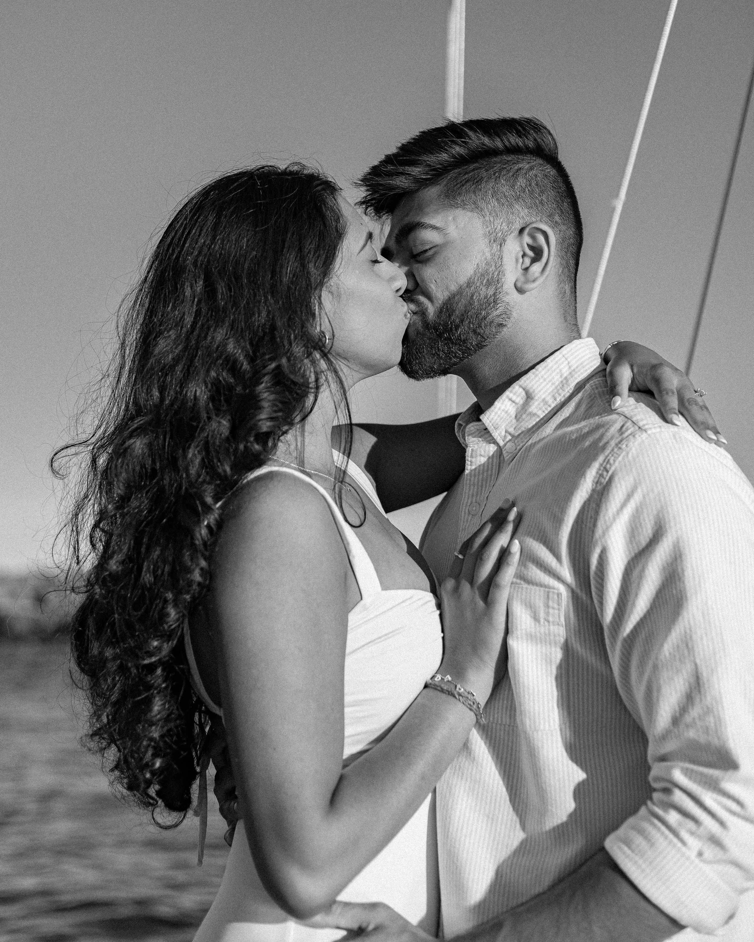 A couple sharing a kiss outdoors, the woman with long wavy hair and the man with short hair and beard, dressed casually.