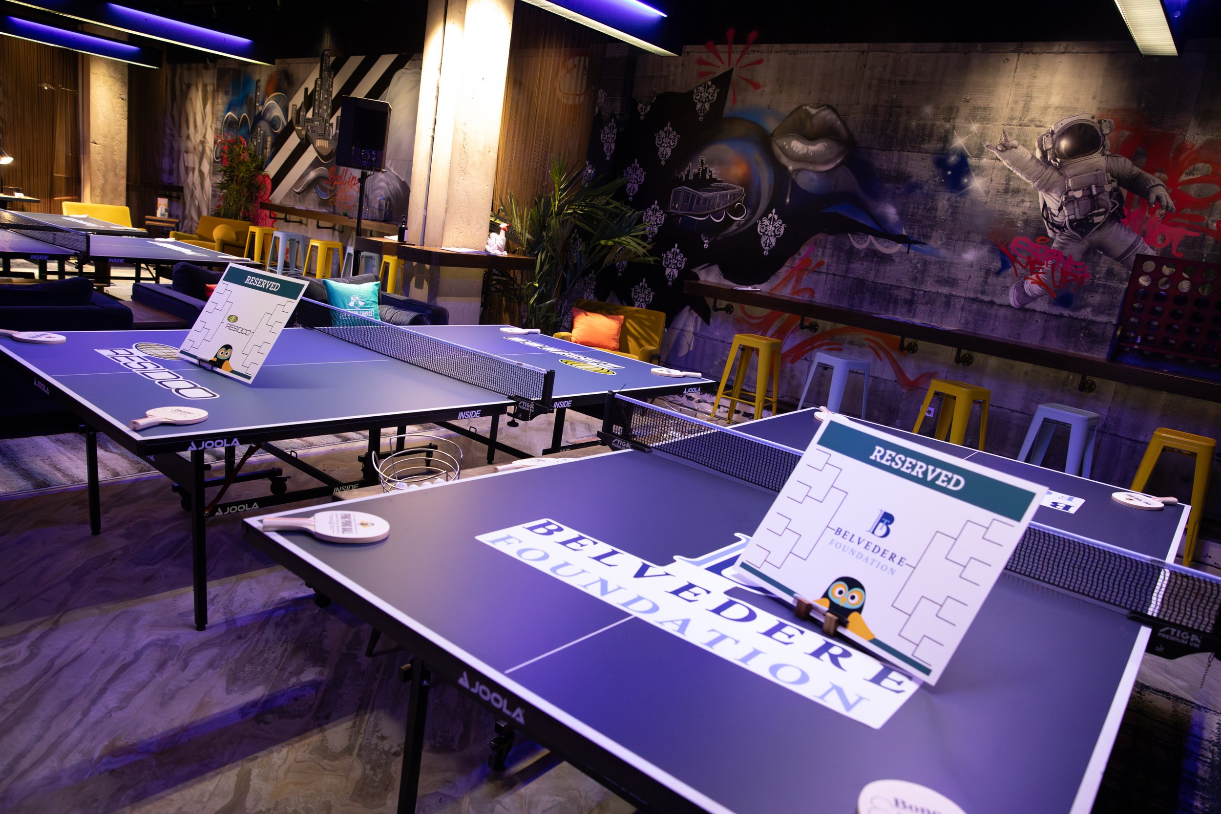 Indoor ping pong club with tables and colorful wall art.