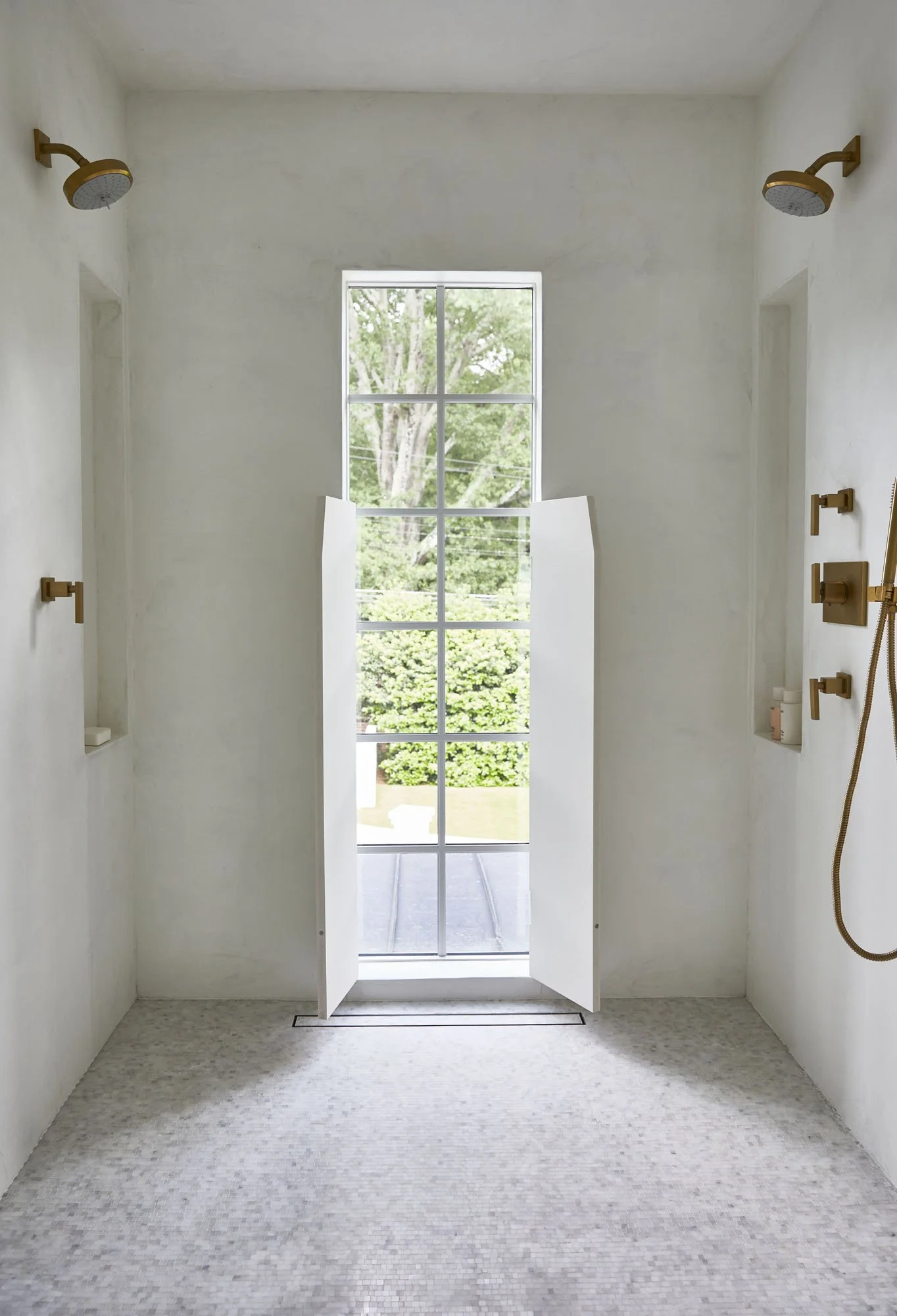 K. Interiors Design Work - A white tiled shower with a window and outdoor greenery visible through a set of white shutters.