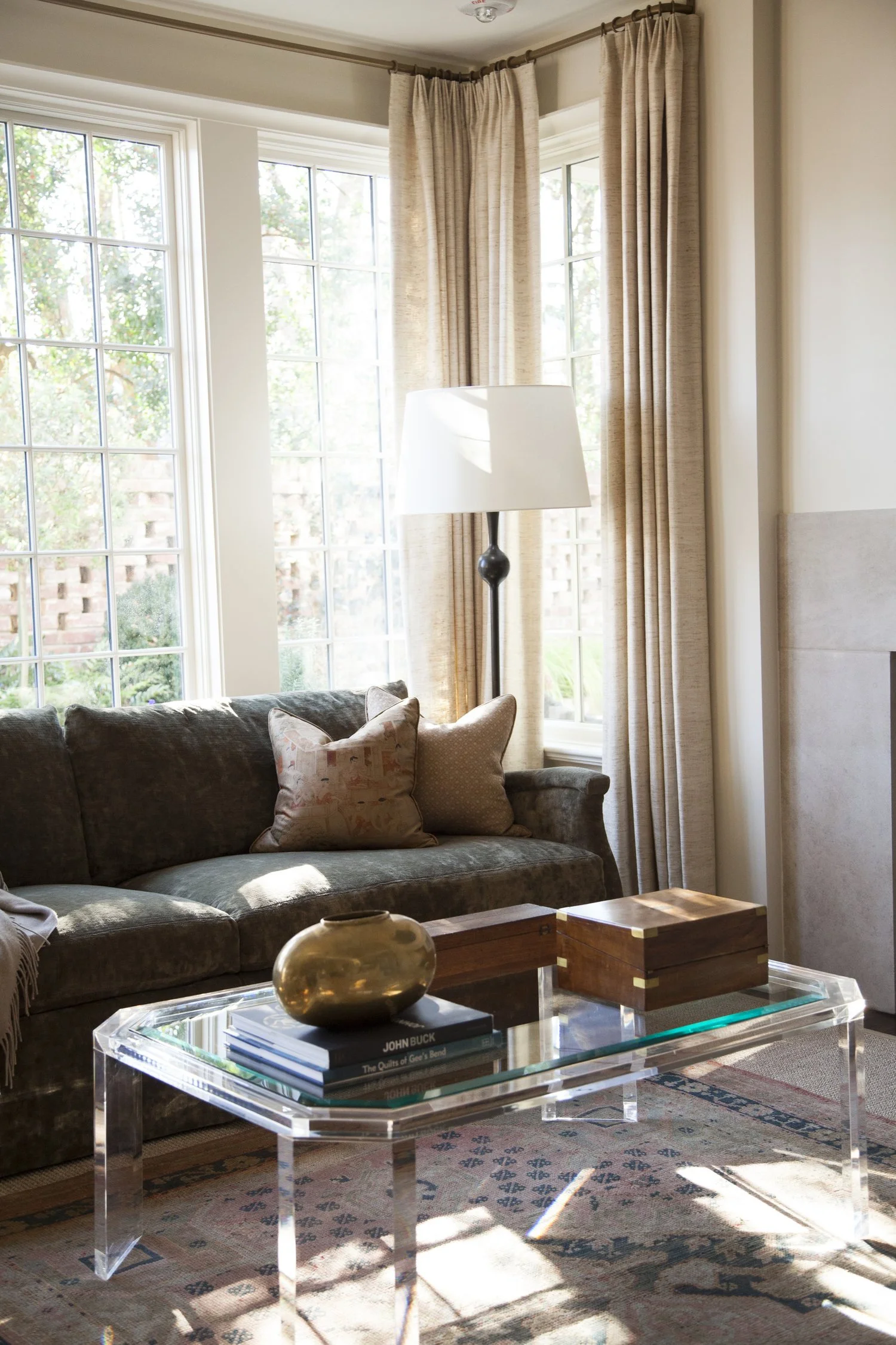 K. Interiors Design Work - Living room with a dark green velvet sofa, beige curtains, and a glass coffee table with decorative items.