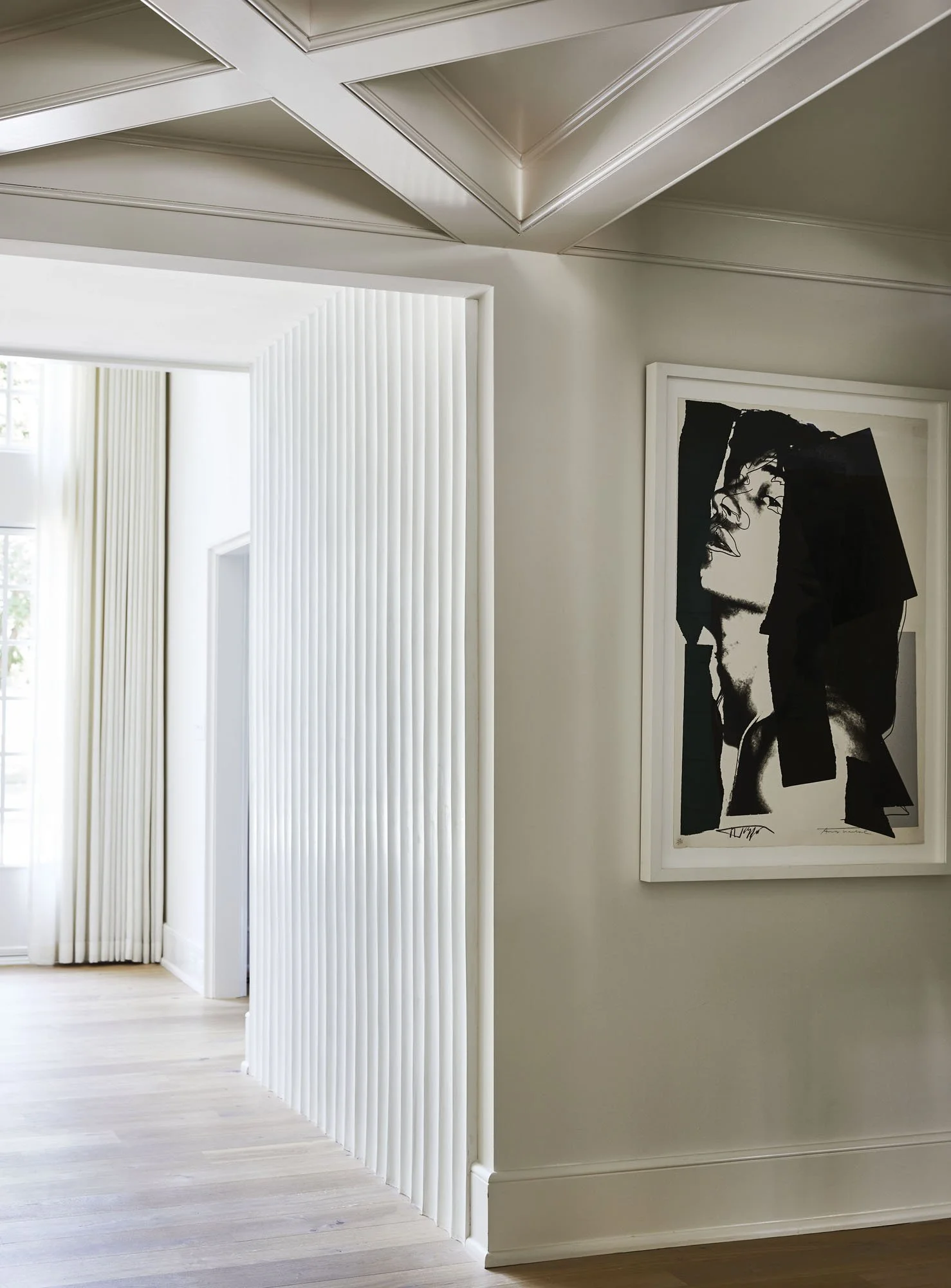 K. Interiors Design Work - Interior of a modern home with a hallway, white walls, and a black and white art print of a woman's face on the wall.