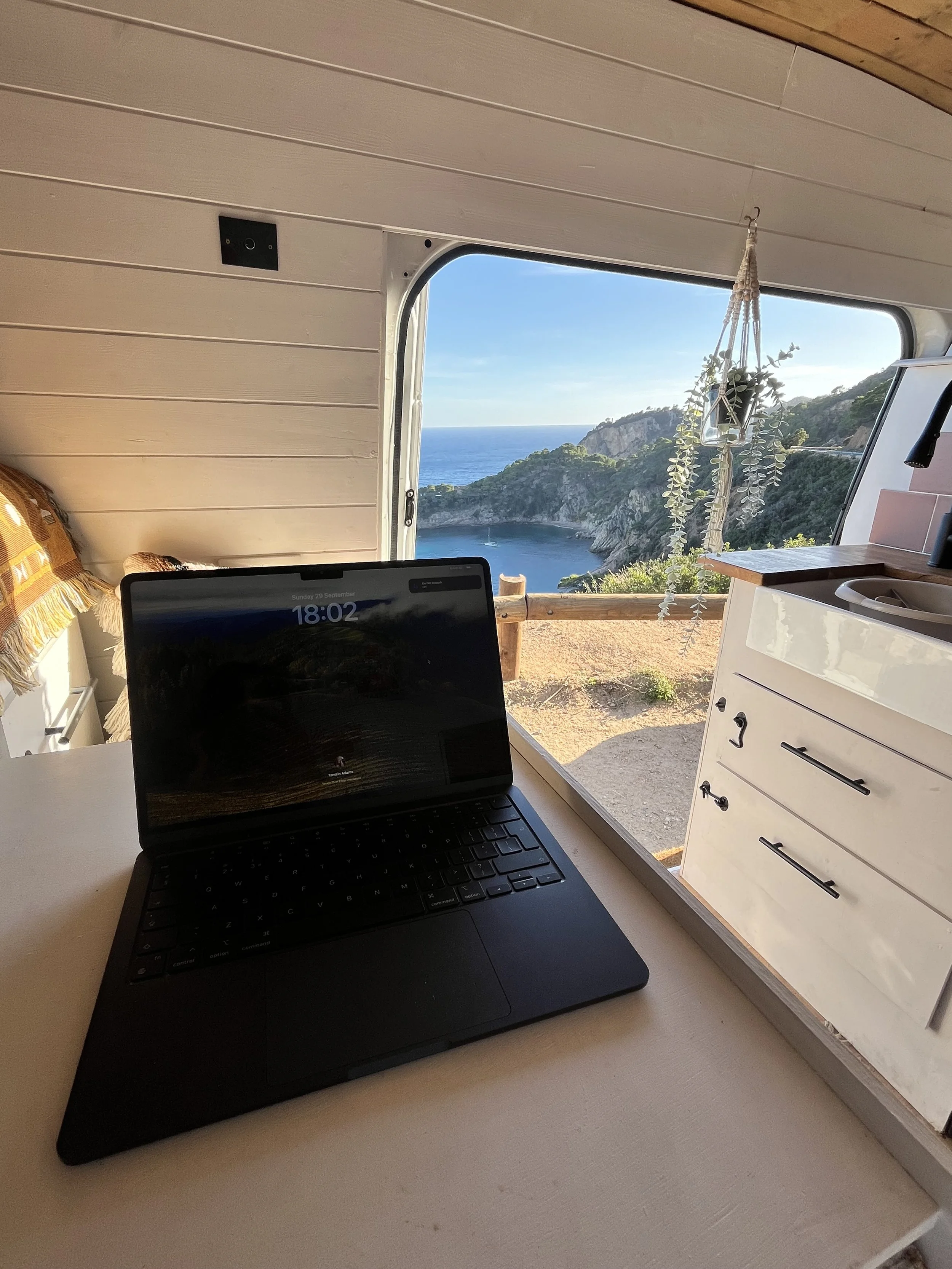 A laptop sits open inside a converted van with the sliding door open to reveal a coastal view