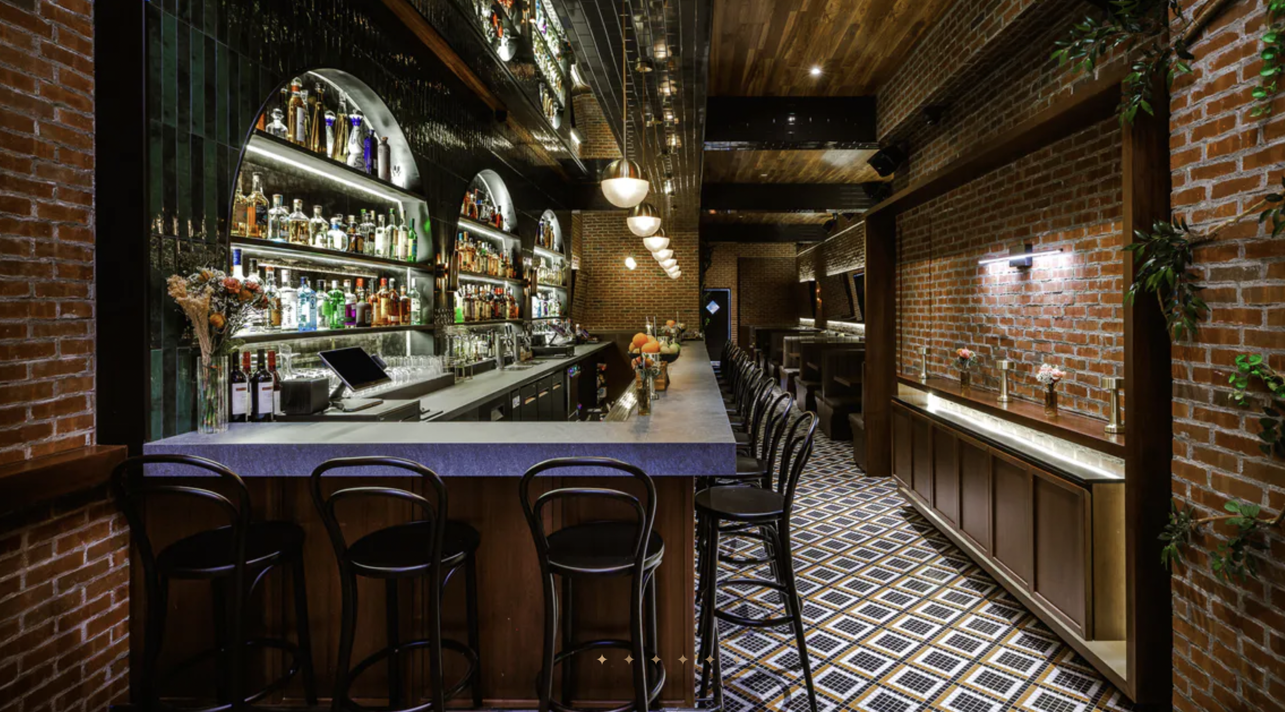 Interior of stylish bar Katherine, in midtown Manhattan, with a white marble counter, black stools, brick walls, decorative plants, and a black ceiling with pendant lights. Venue and Brand Design by Skyscraper Creative.