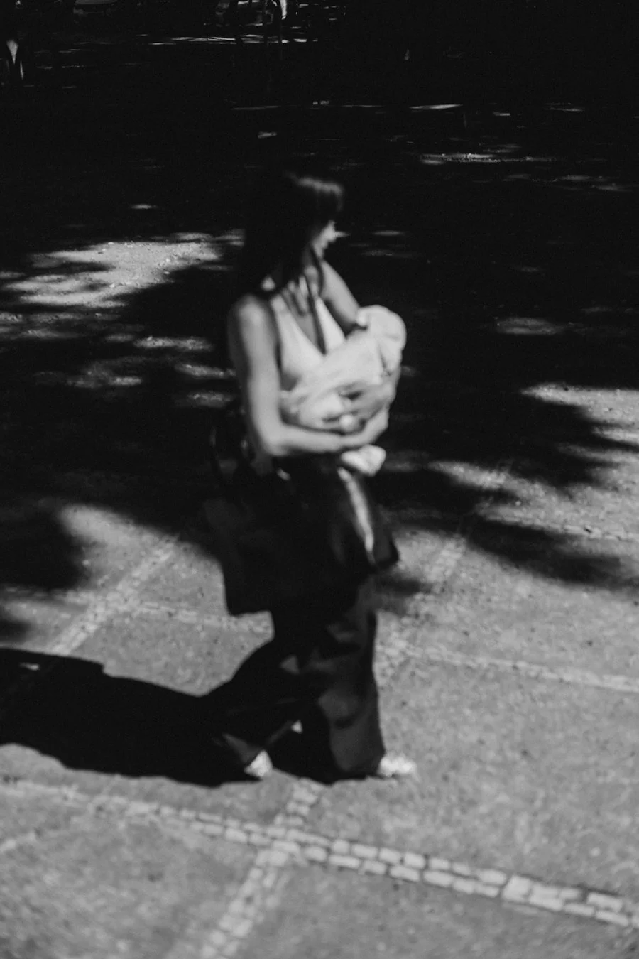 A woman holding a small dog, standing on a sidewalk at night, shadows cast on the ground.