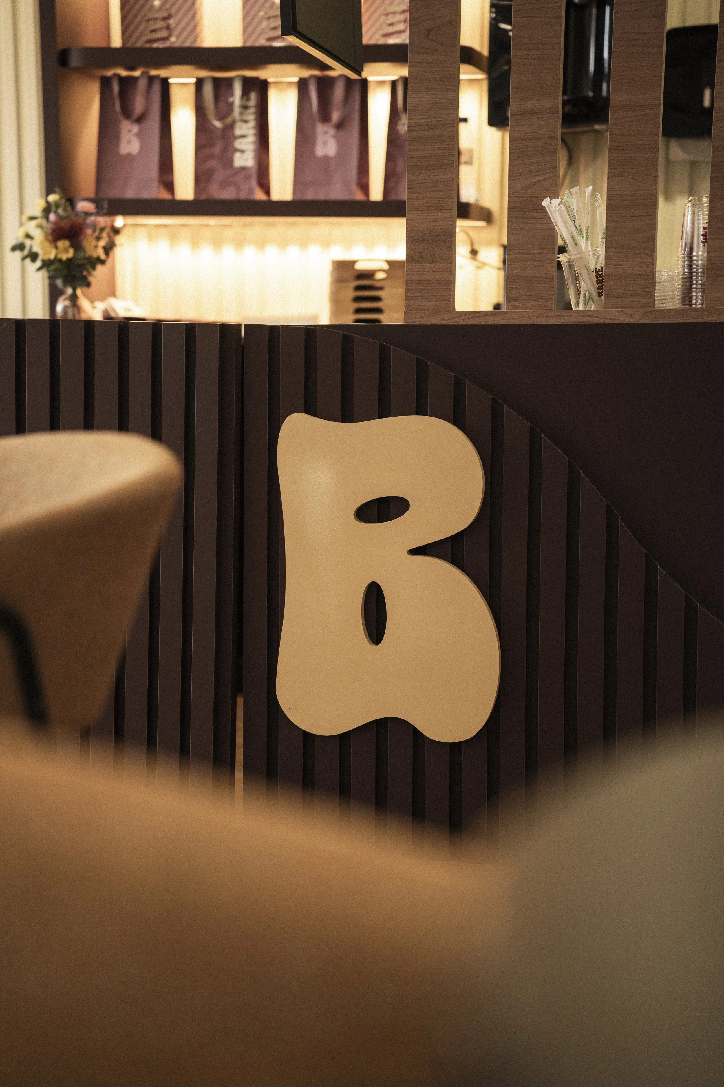 Close-up of a coffee shop counter with a large beige bear-shaped decor, straw packets, and clear plastic cups in the background.