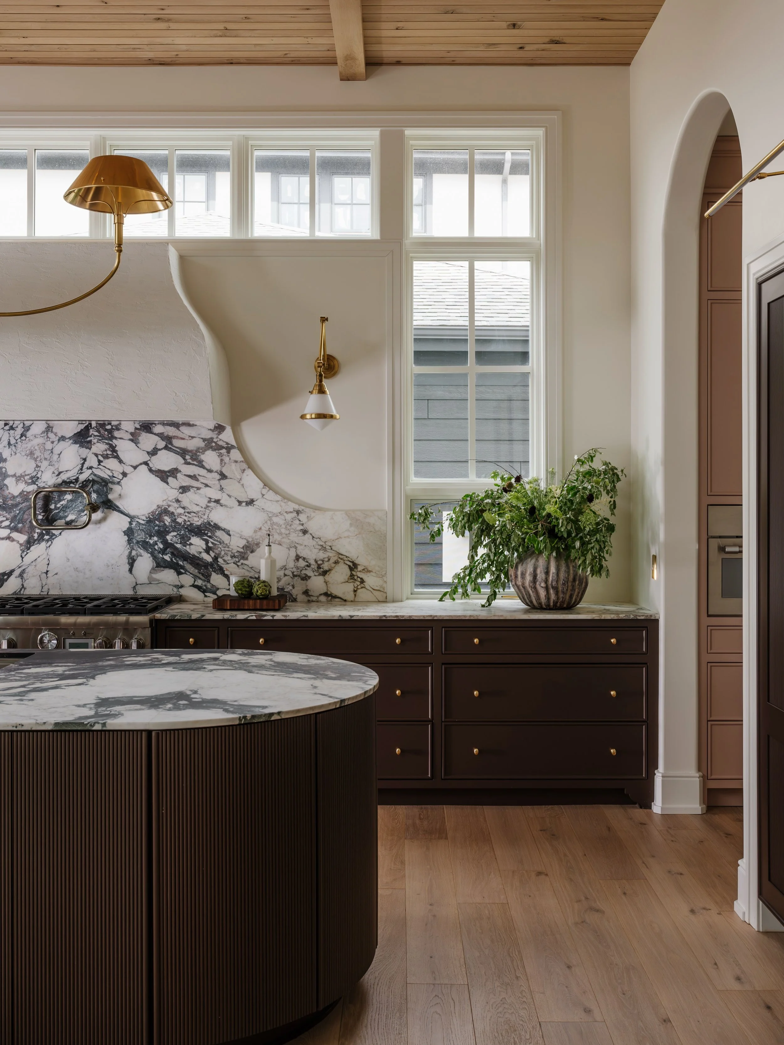 A closer look at the heart of Oxbow Manor, the kitchen!

We layered rich brown cabinetry with a warm white oak ceiling, unlacquered brass, plaster, and beautiful Viola marble to create a space full of warmth and character. One of my favorite architec