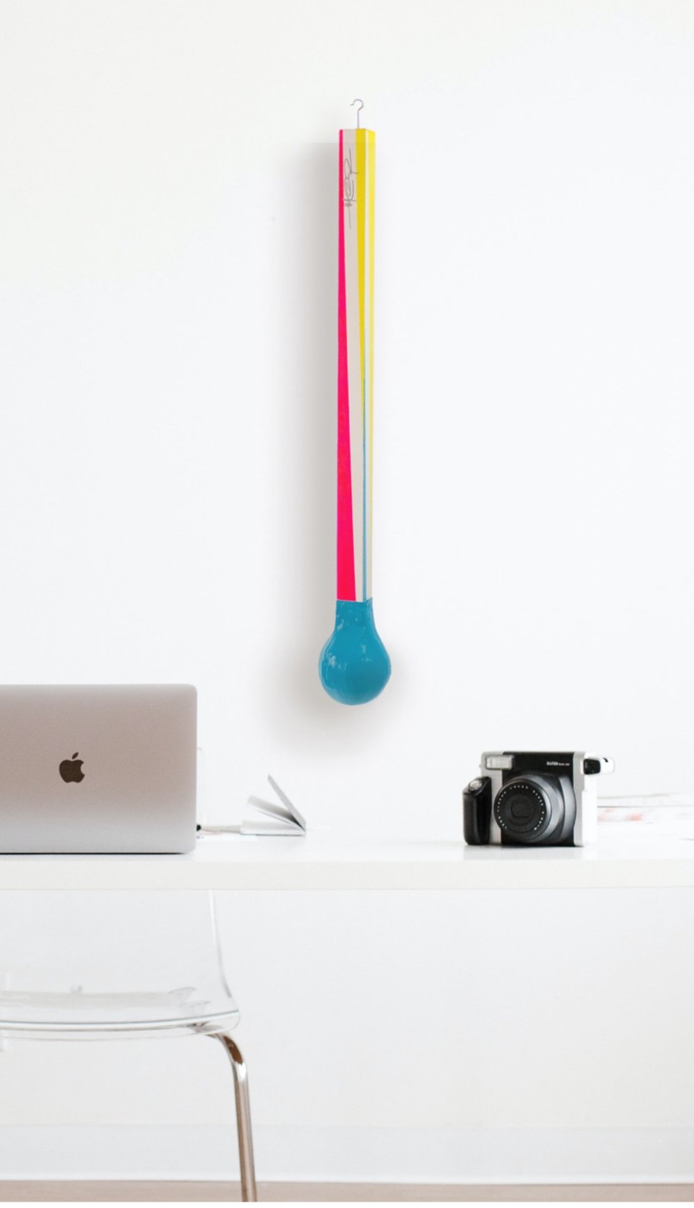 Minimalist white workspace with a laptop, camera, and colorful thermometer decoration on the wall.