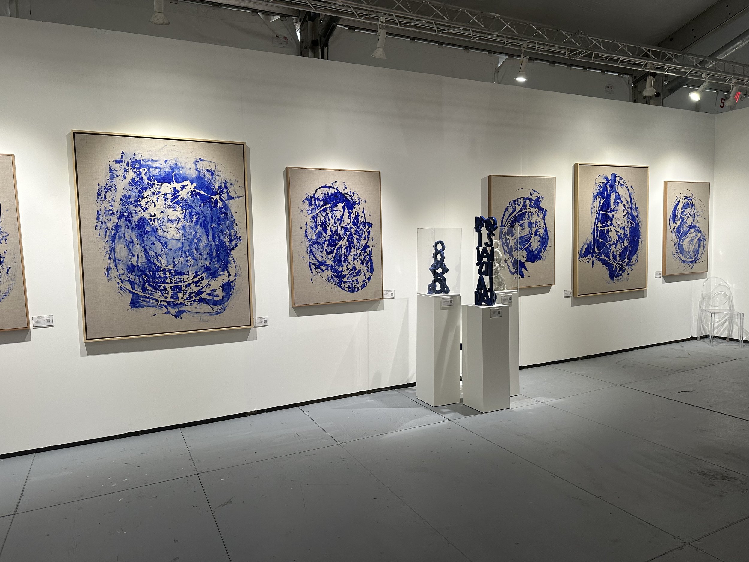 Gallery with abstract blue paintings on canvas and letter sculptures on pedestals.