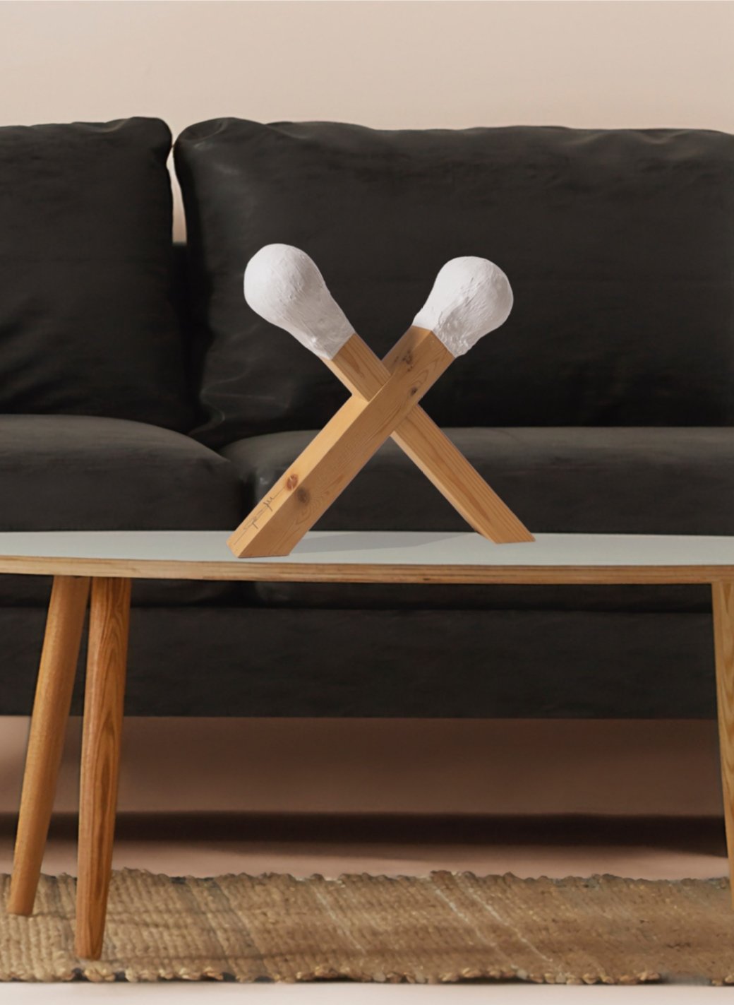 Decorative crossed wooden sticks resembling matchsticks on a coffee table with a black sofa in the background.