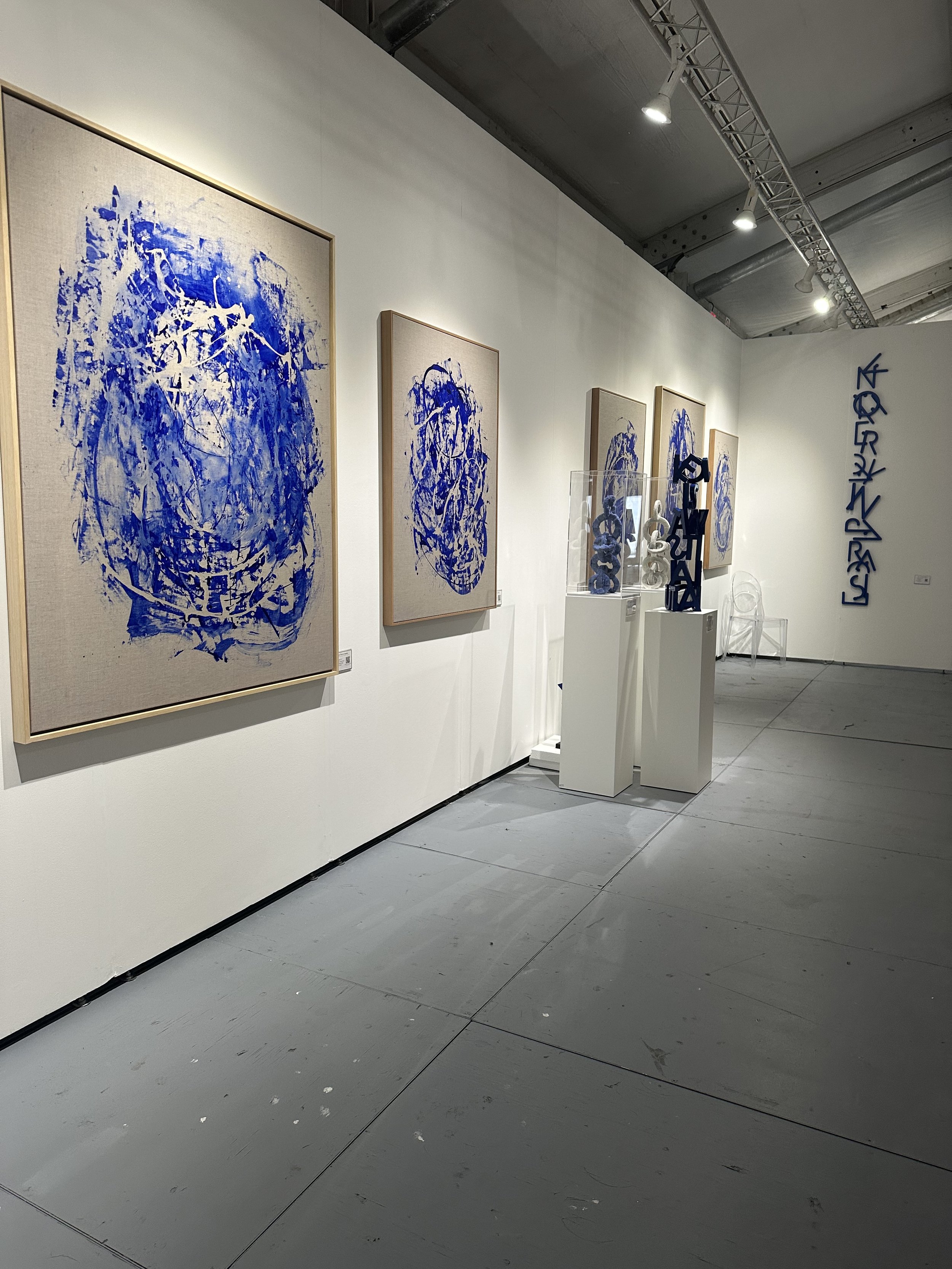 Art gallery featuring abstract paintings with blue patterns on canvas and sculptural pieces displayed on pedestals.