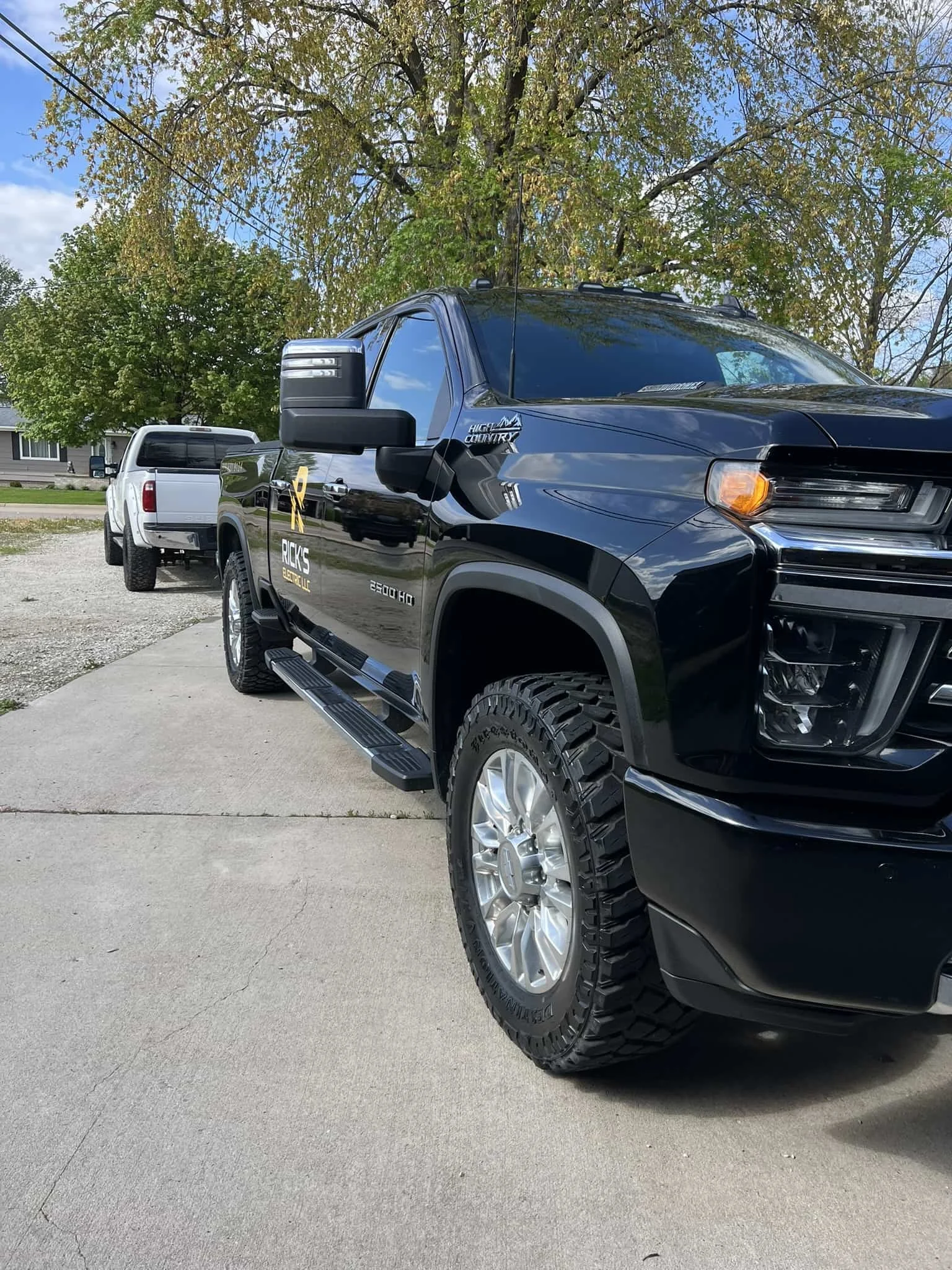 Black pickup truck with decals parked on a concrete driveway in front of a tree with green leaves and a blue sky.