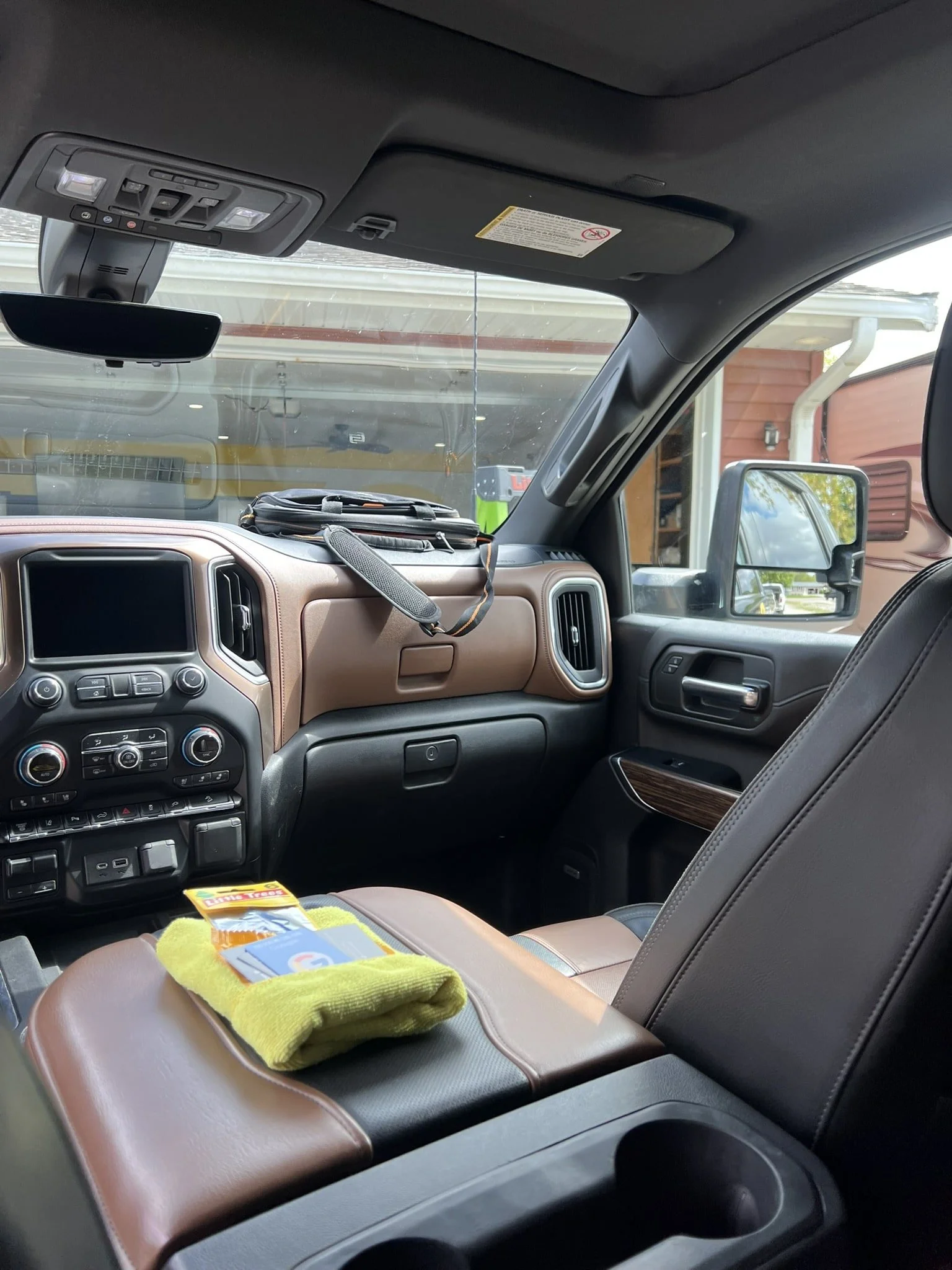 Interior of a vehicle's front cabin showing the dashboard, steering wheel, passenger seat, side mirror, and a pouch on the dashboard. The dashboard has a brown and black color scheme, with various control buttons and vents.