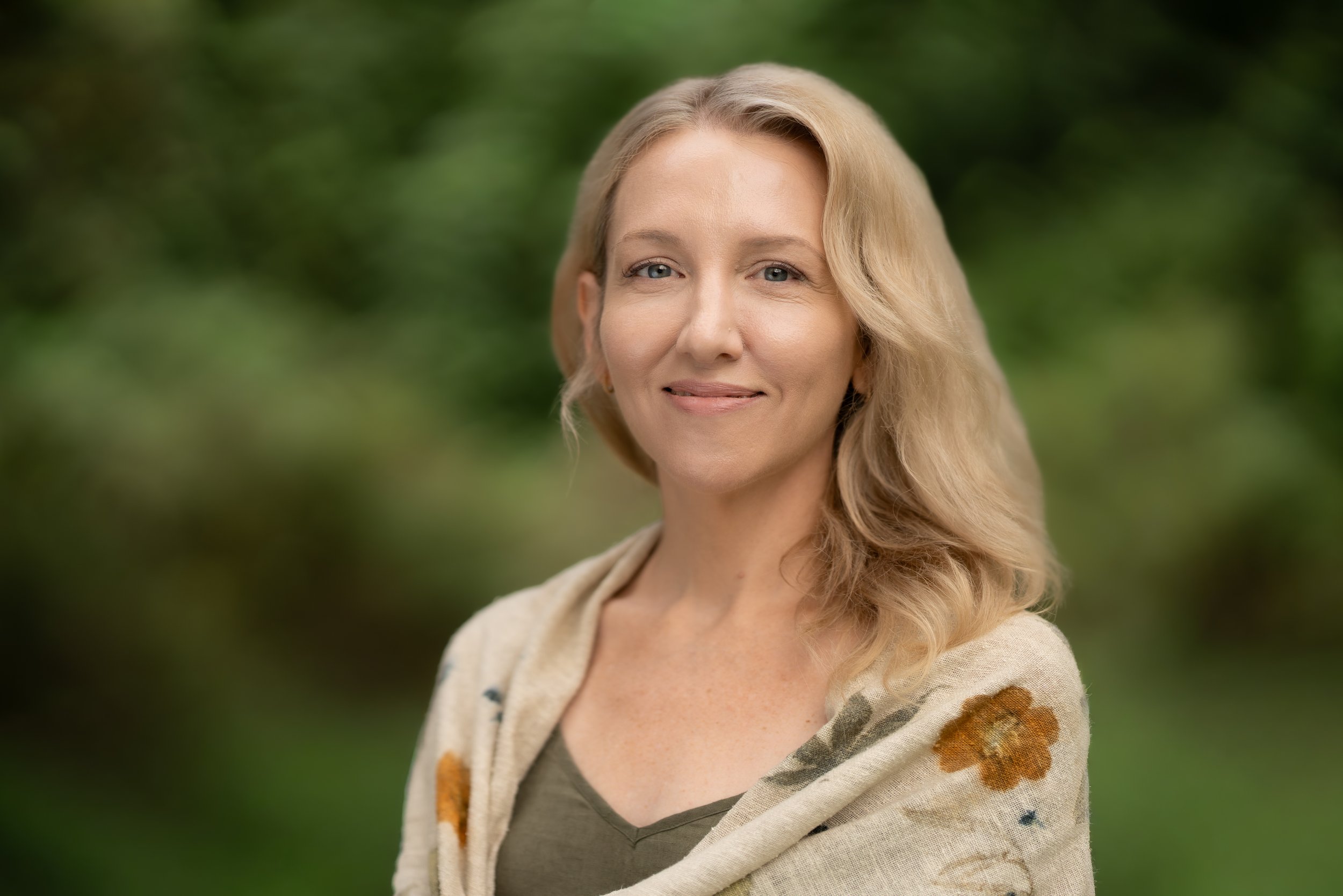 A smiling Waldorf school Director standing outdoors with green foliage in the background.