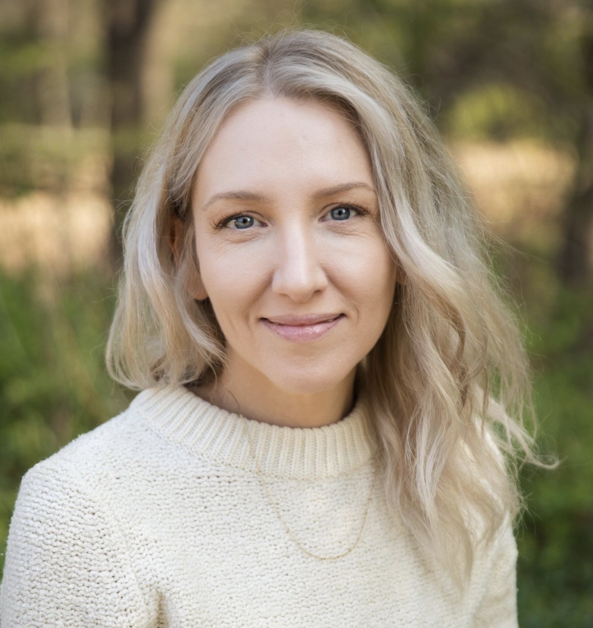 A smiling Waldorf school Director standing outdoors with green foliage in the background.