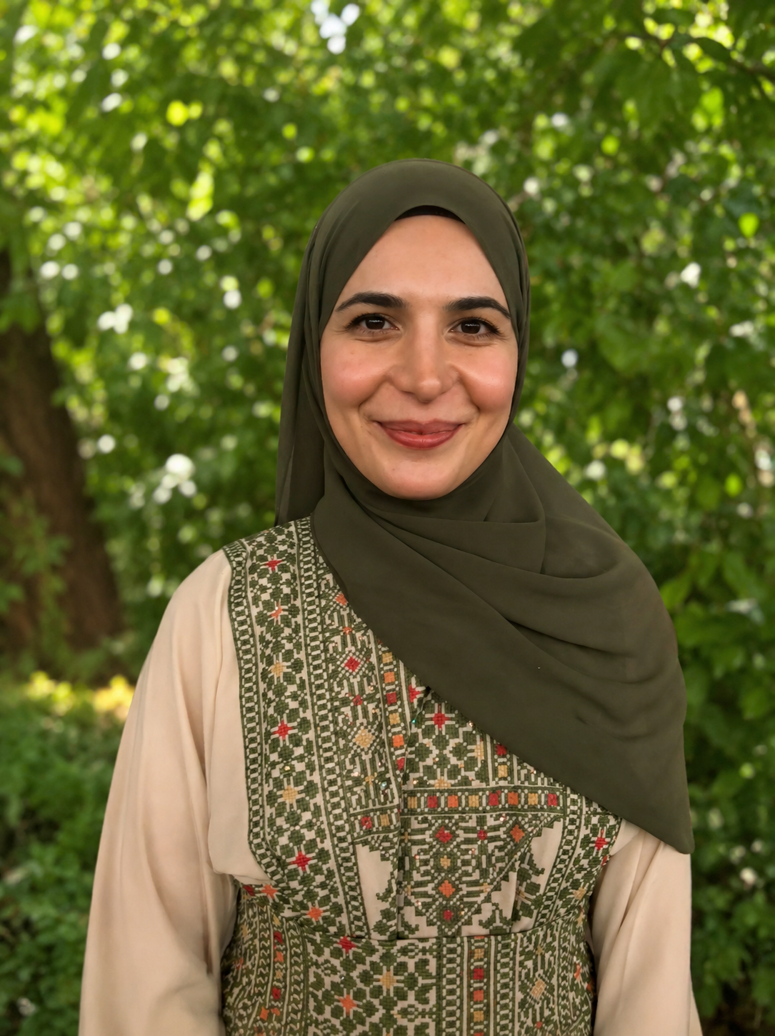 A smiling Forest Kindergarten Waldorf teacher standing outdoors with green foliage in the background.