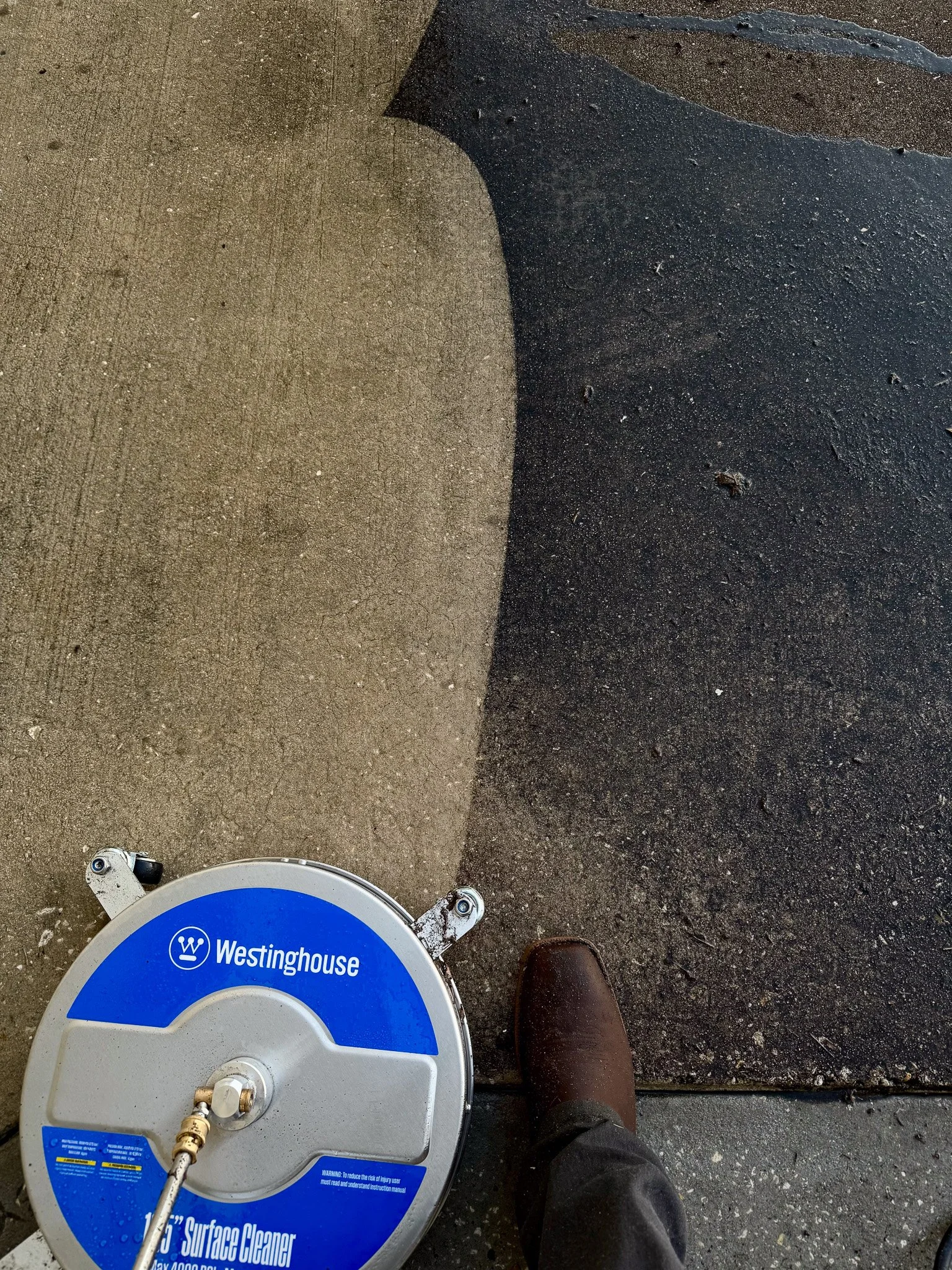 Top-down view of a person wearing brown shoes cleaning a concrete sidewalk with a Westinghouse surface cleaner, showing a clean and dirty area.