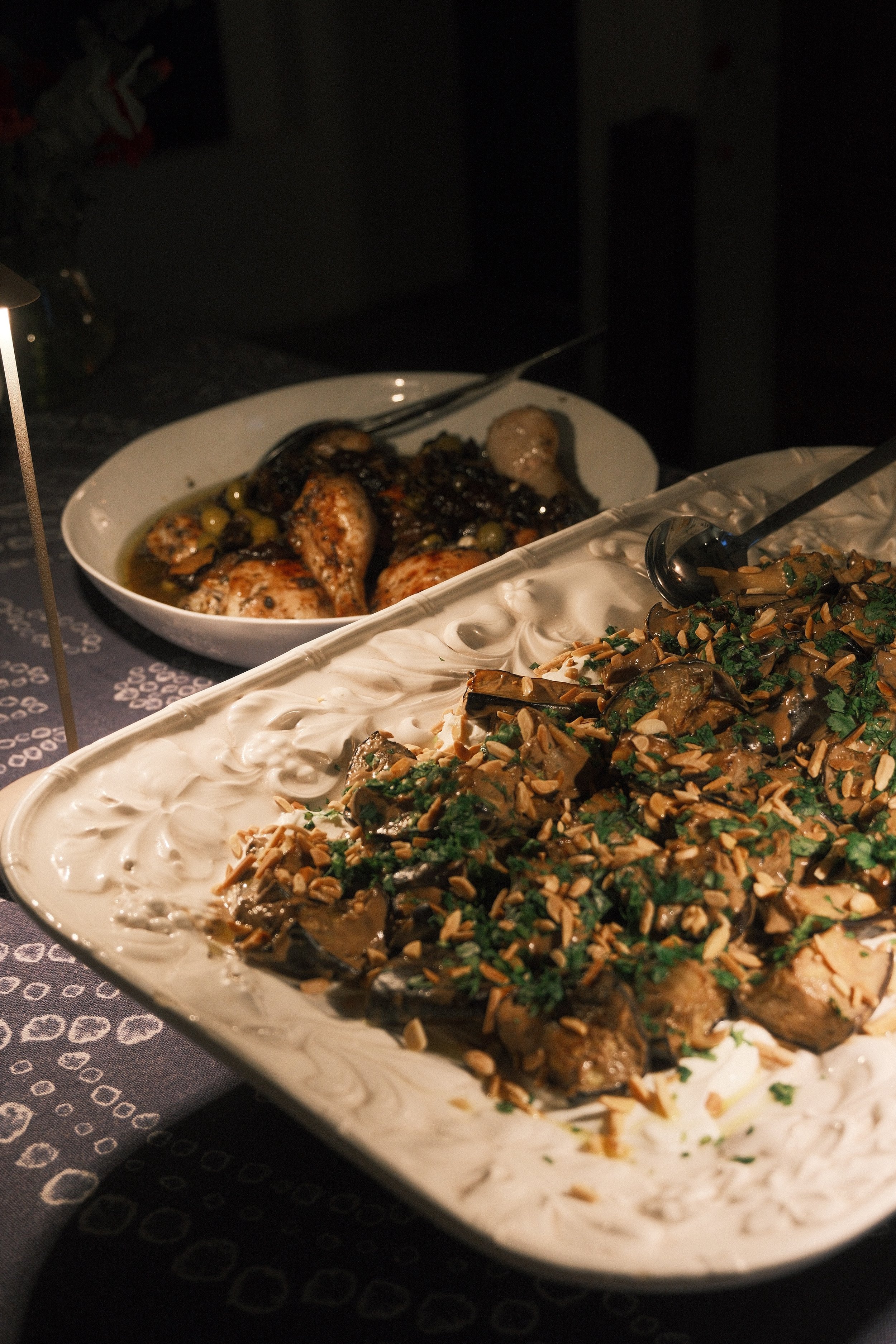 A white oval dish with cooked chicken drumsticks topped with chopped nuts and herbs, and a creamy white sauce.