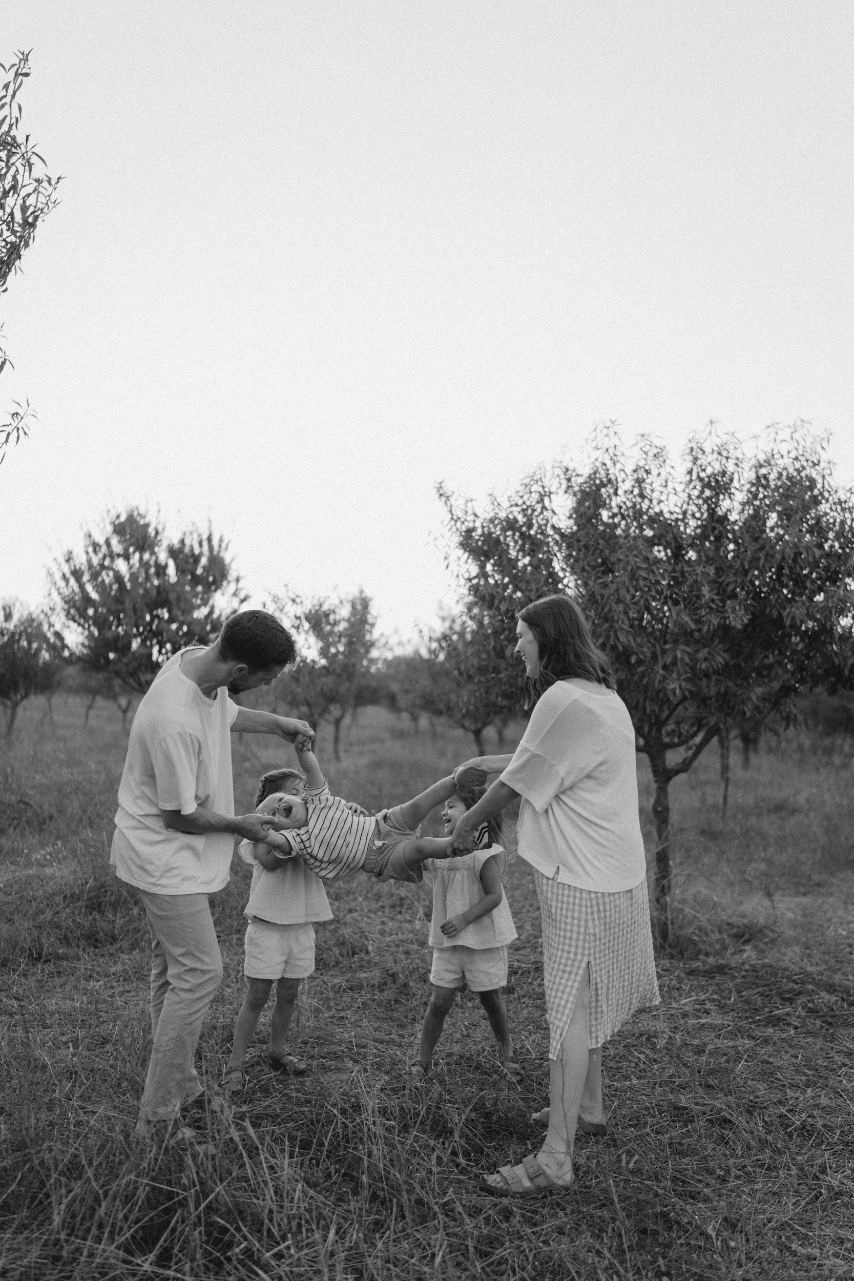 Una familia tiene diversión en un campo con árboles, jugando con los niños.