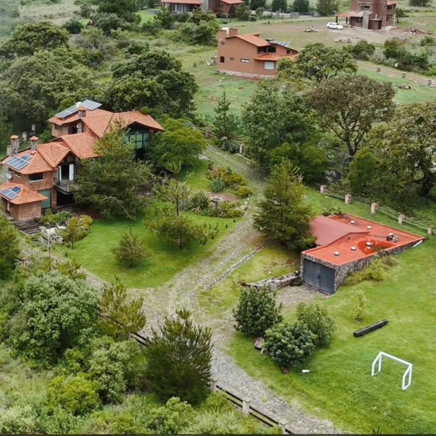 Viviendas residenciales rodeadas de árboles y áreas verdes, con caminos de piedra y un campo con portería de fútbol.