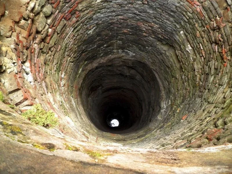 Pozo profundo de piedra, visto desde arriba, con luz en el fondo.