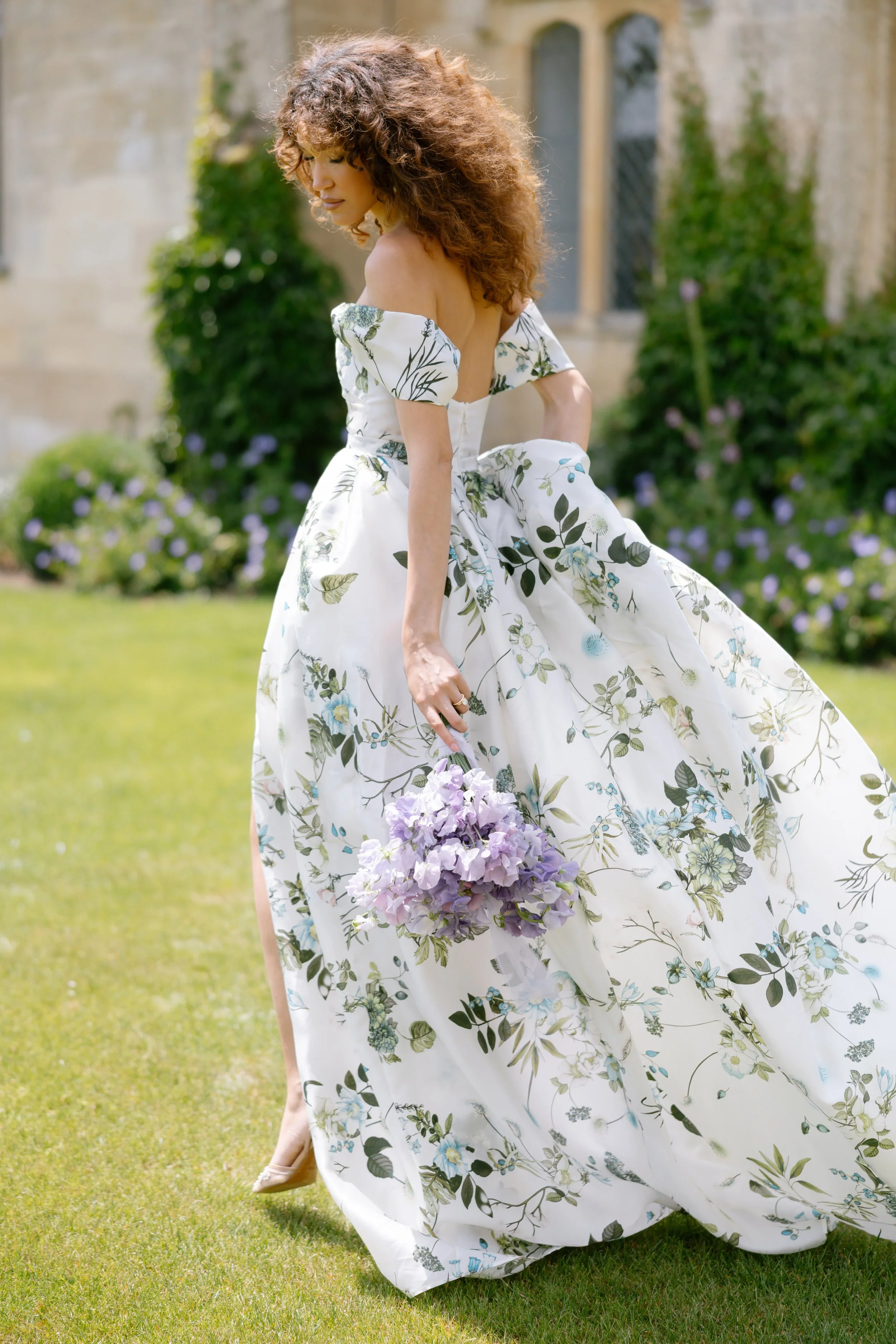 Woman in a pink bridal gown posing in front of a "Mara Marie Bridal" sign, surrounded by white floral arrangements.