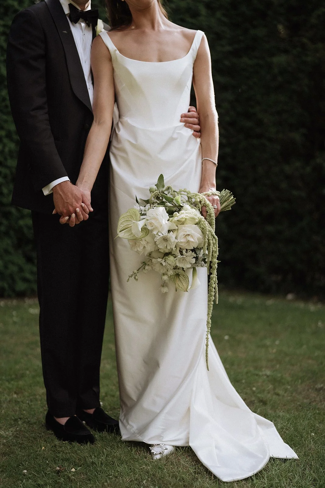Outdoor wedding ceremony setup with white chairs and floral decorations, featuring an ivy-covered archway with white and yellow flowers. Cotswolds, Oxfordshire, Wedding Florist. 