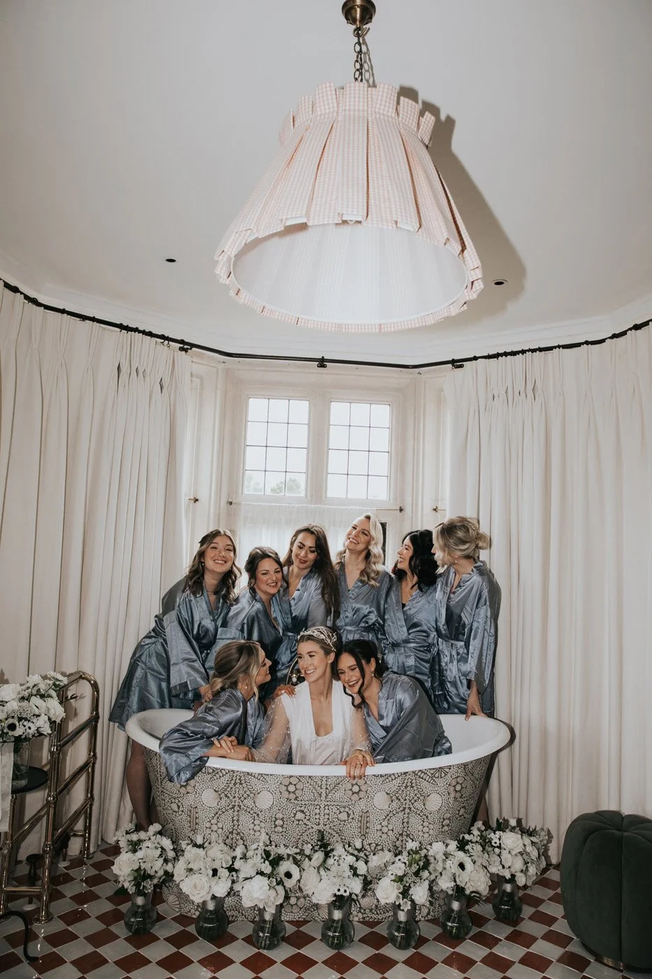 Group of women wearing robes posing in a decorative bathtub surrounded by white flowers in the Kin House bridal suite, Kin House, Wiltshire, florist.