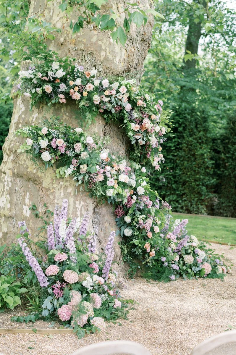 Tree with decorative floral arrangements featuring pastel-colored flowers and green foliage at Avington Park, Wiltshire, Wedding Florist.