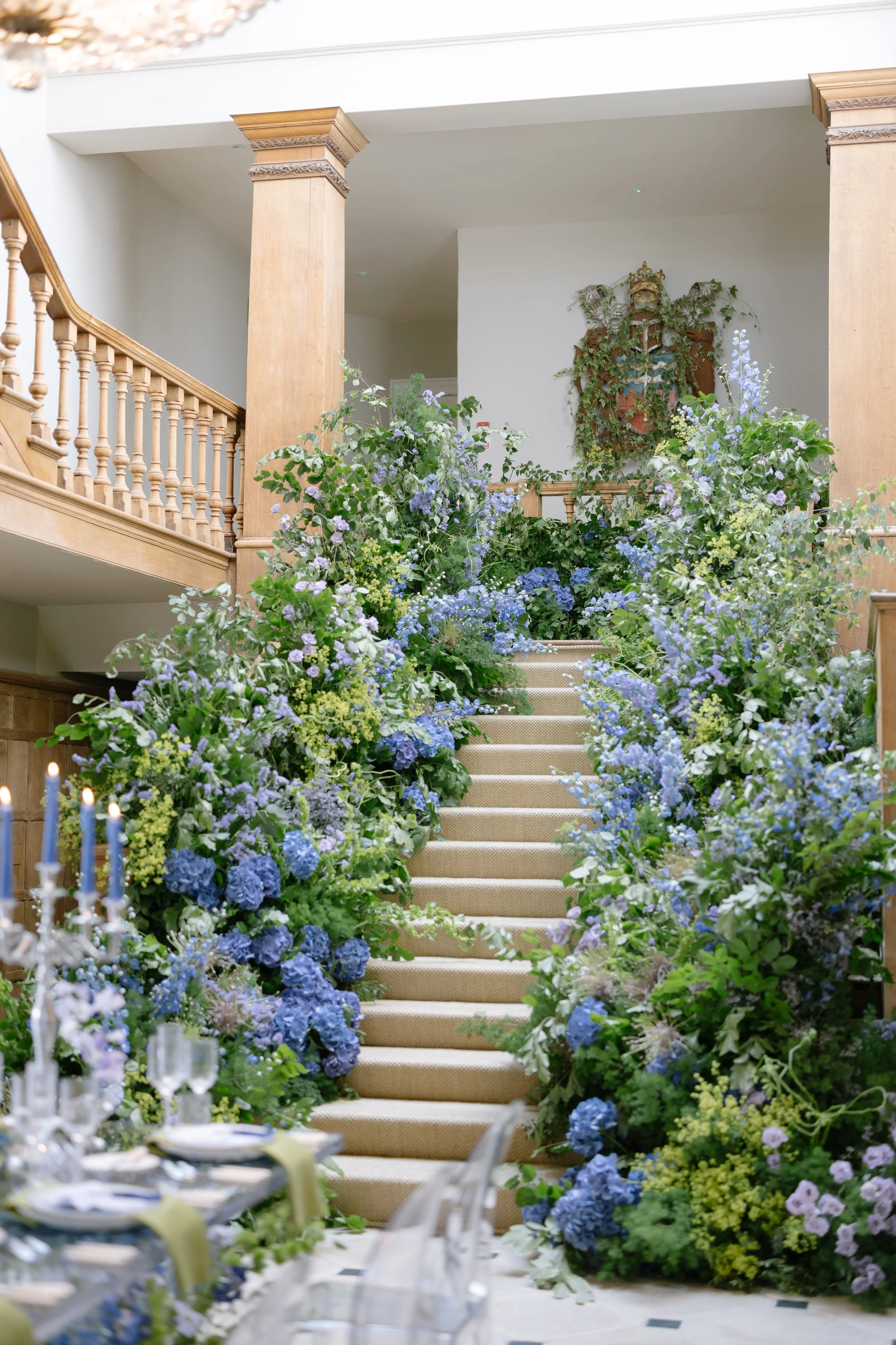 Bride and groom walking down the aisle at an outdoor wedding, surrounded by guests clapping and taking photos, with floral decorations and greenery in the background. Oxfordshire wedding, wedding florist. 