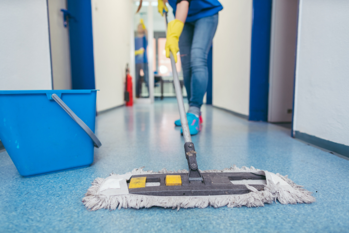 Person mopping a blue floor in a hallway, with a blue bucket nearby.