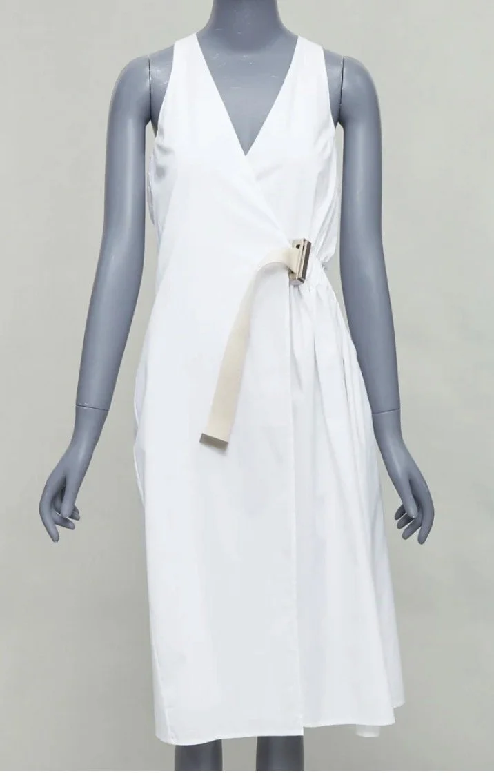 A white sleeveless dress with a V-neck, displayed on a gray mannequin, featuring a fabric belt with a rectangular buckle.