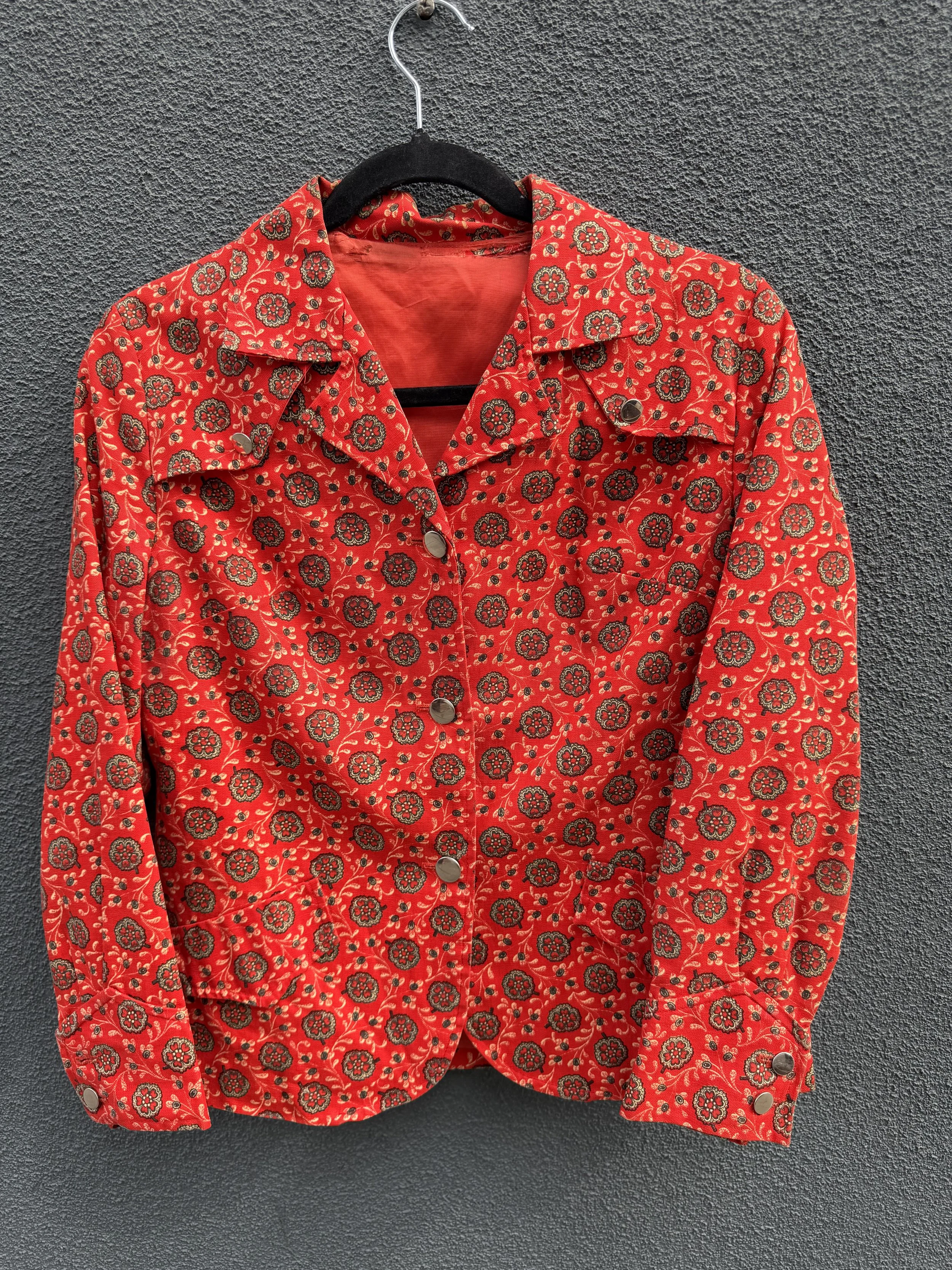 Red button-up shirt with black floral pattern hanging on a black hanger against a gray textured wall.