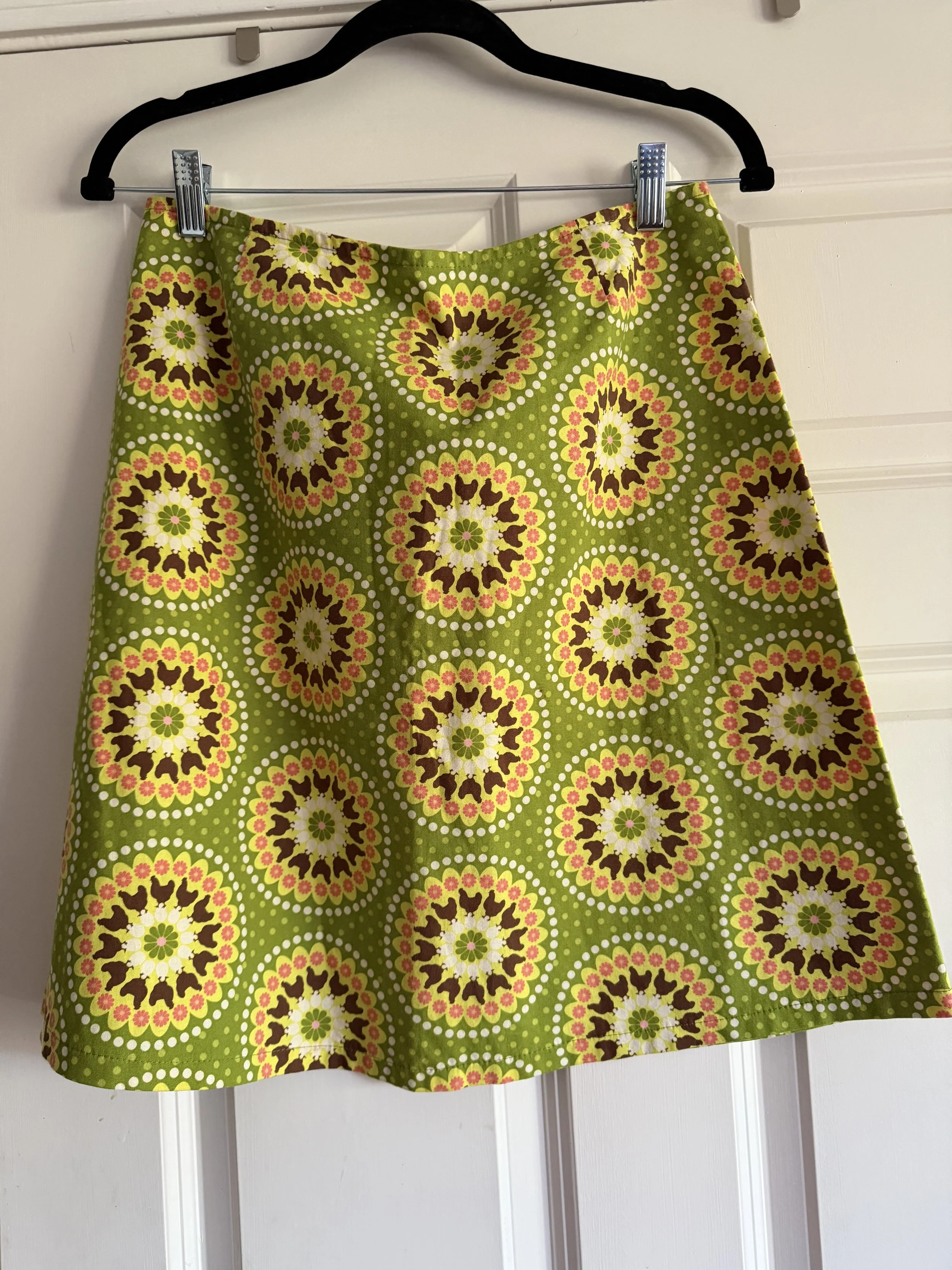 A green skirt with a circular floral pattern hanging on a black hanger against a white door.