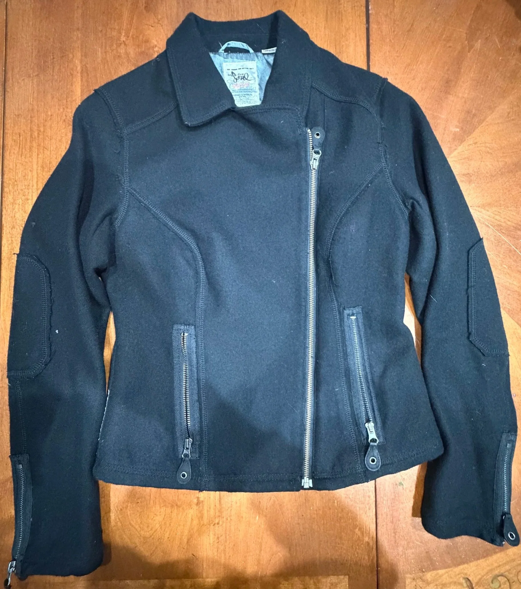 Black jacket with multiple zippers, lying on a wooden bed or floor.
