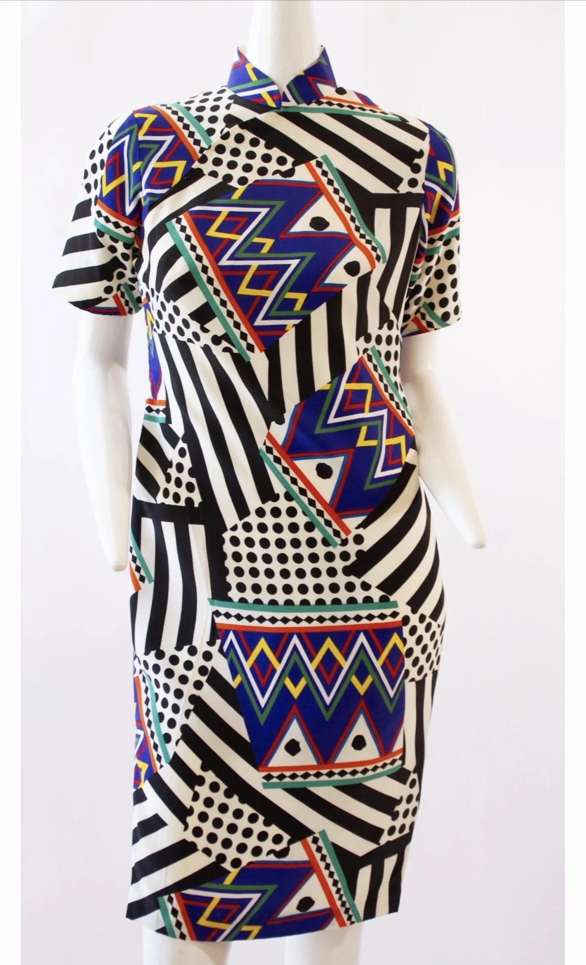 A mannequin dressed in a colorful, abstract patterned dress with geometric designs, stripes, polka dots, and zigzags in bold colors like blue, red, yellow, black, and white.