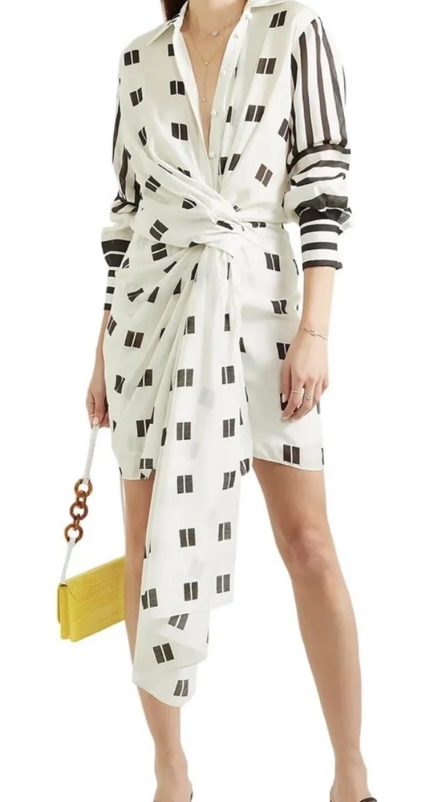 A woman wearing a white shirt and skirt with black geometric patterns, holding a yellow handbag with a chain strap.