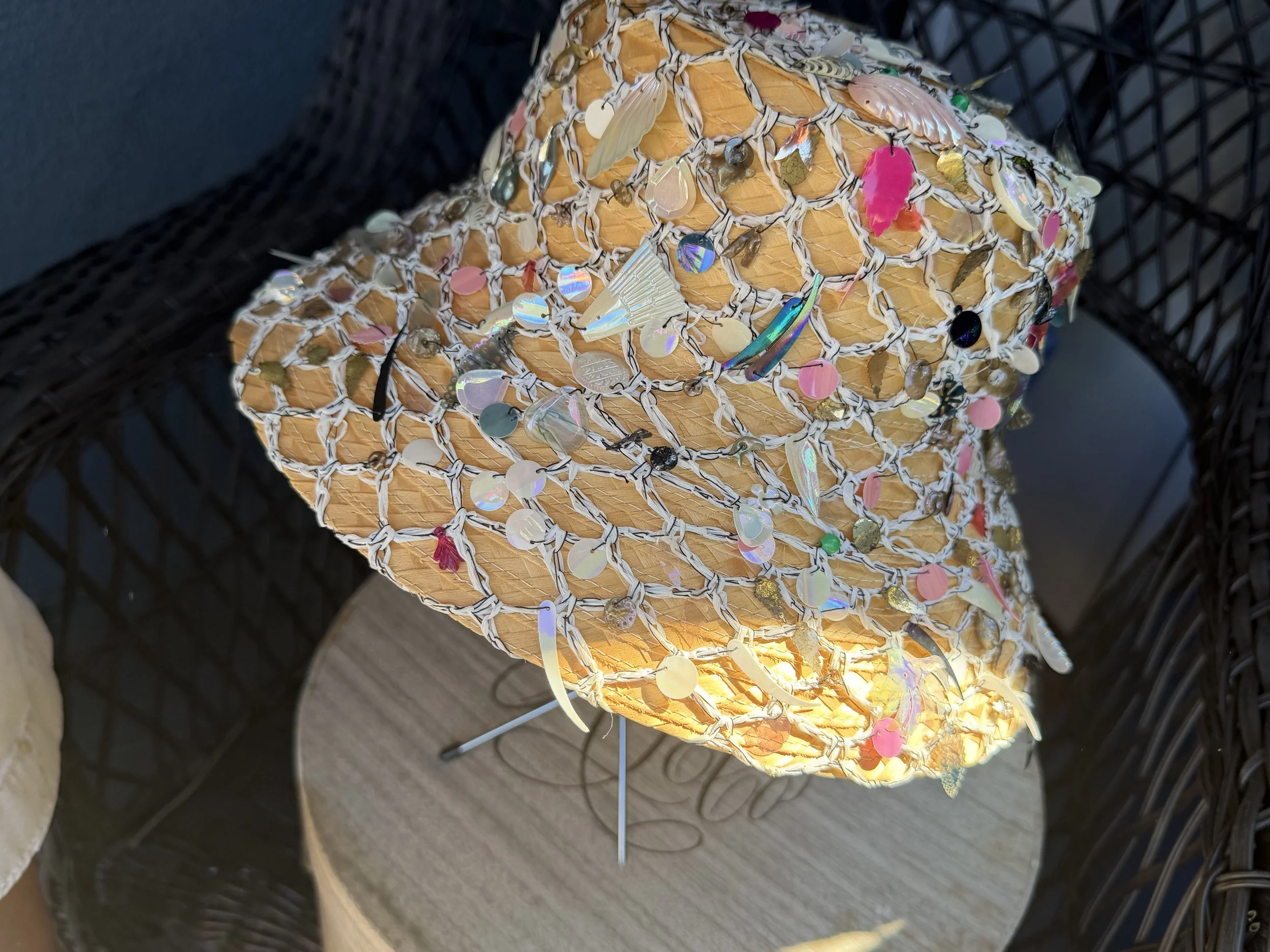 Vintage Betmar Straw Bucket Hat, adorned with various colorful sequins, shells, and beads, sitting on a metal stand on it's vintage hatbox