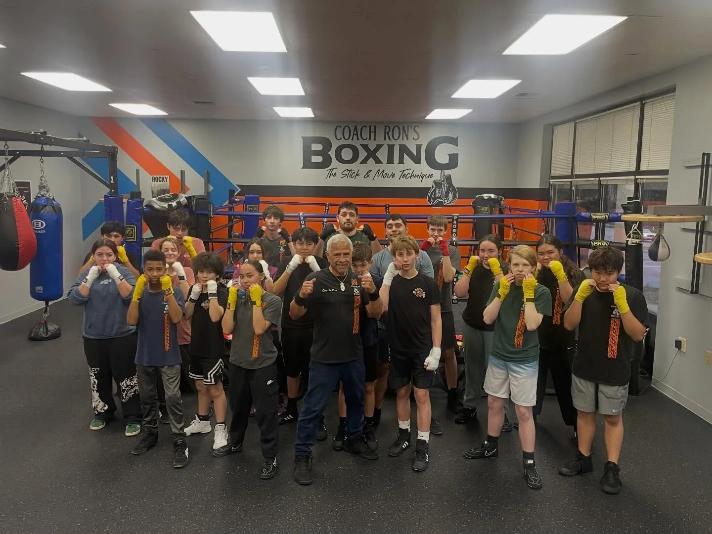 Youth boxing class holding up their wrapped fists in a guard stance with their coach