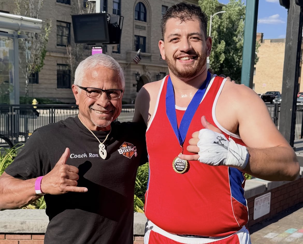 Coach Justin Ah Chan wearing a medal after a bout, standing with Coach Ron