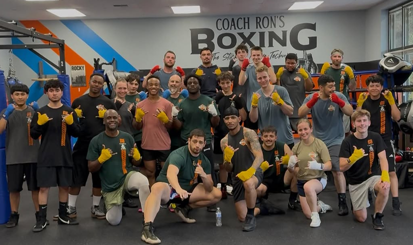 Coach Justin and members posing together in front of Coach Ron's Boxing and ring