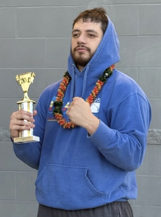 Coach Justin Ah Chan holding a trophy and wearing a lei