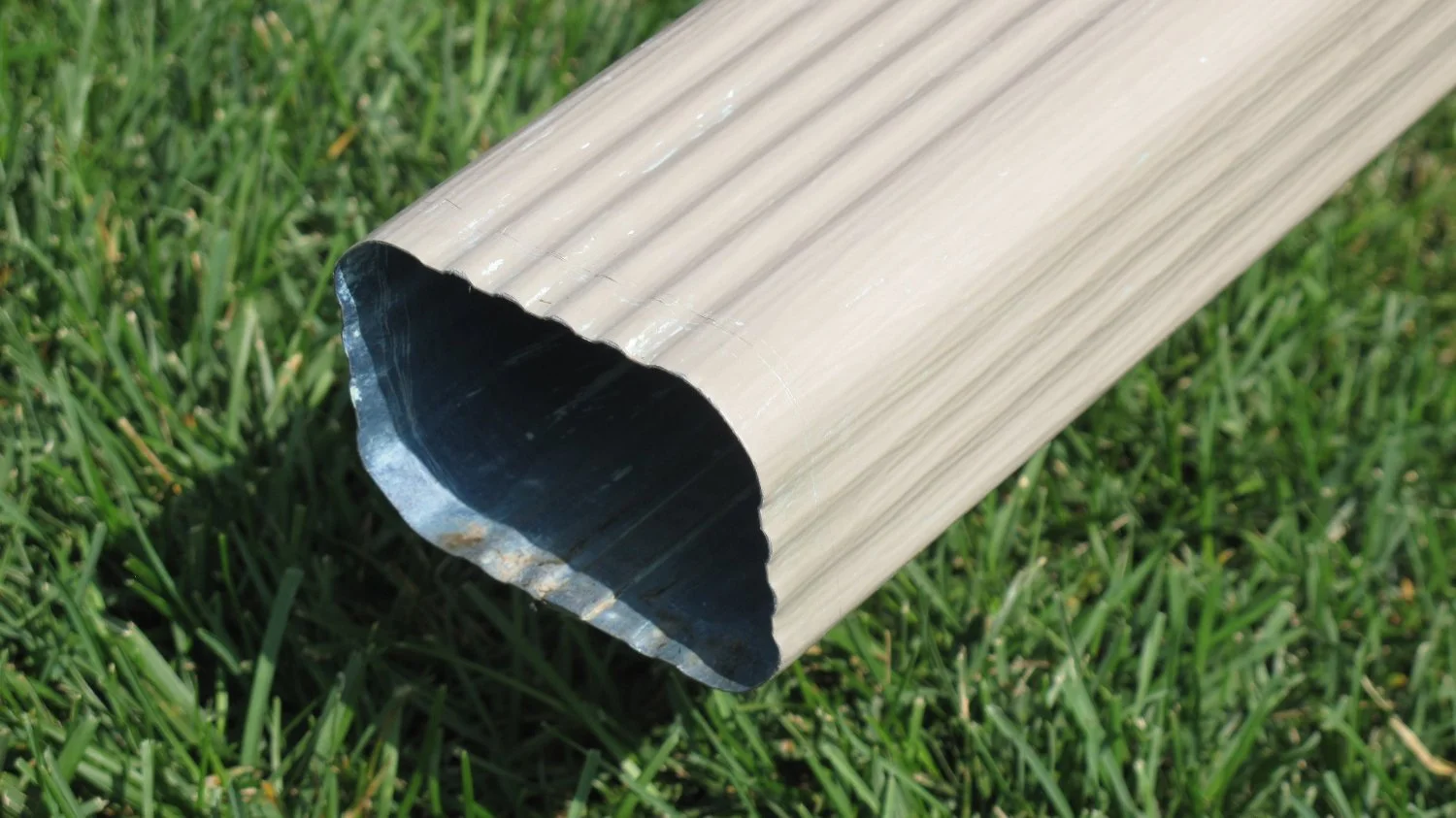 a taupe downspout with sharp edges over a grass lawn background