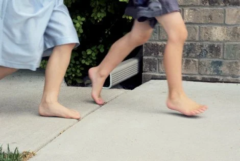 barefoot children running on a sidewalk next to a downspout covered with a SpoutTrim safety cap