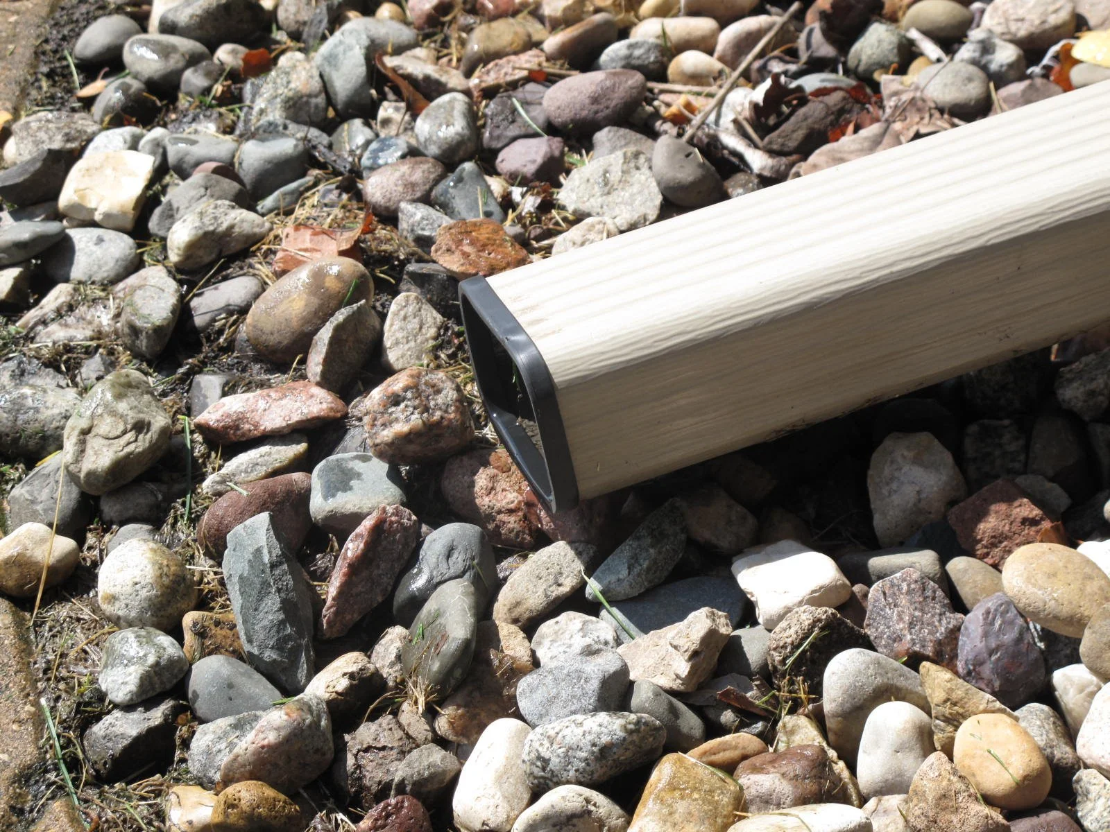 a gutter downspout in a rocky area, covered with a black SpoutTrim cap