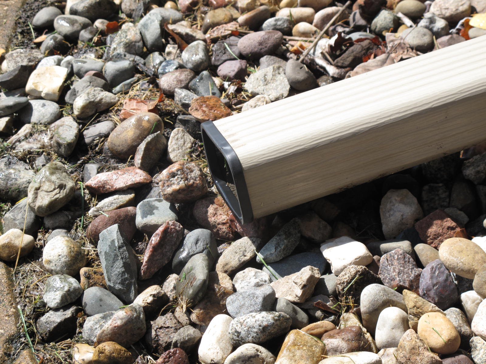 a gutter downspout in a rocky area, covered with a black SpoutTrim cap