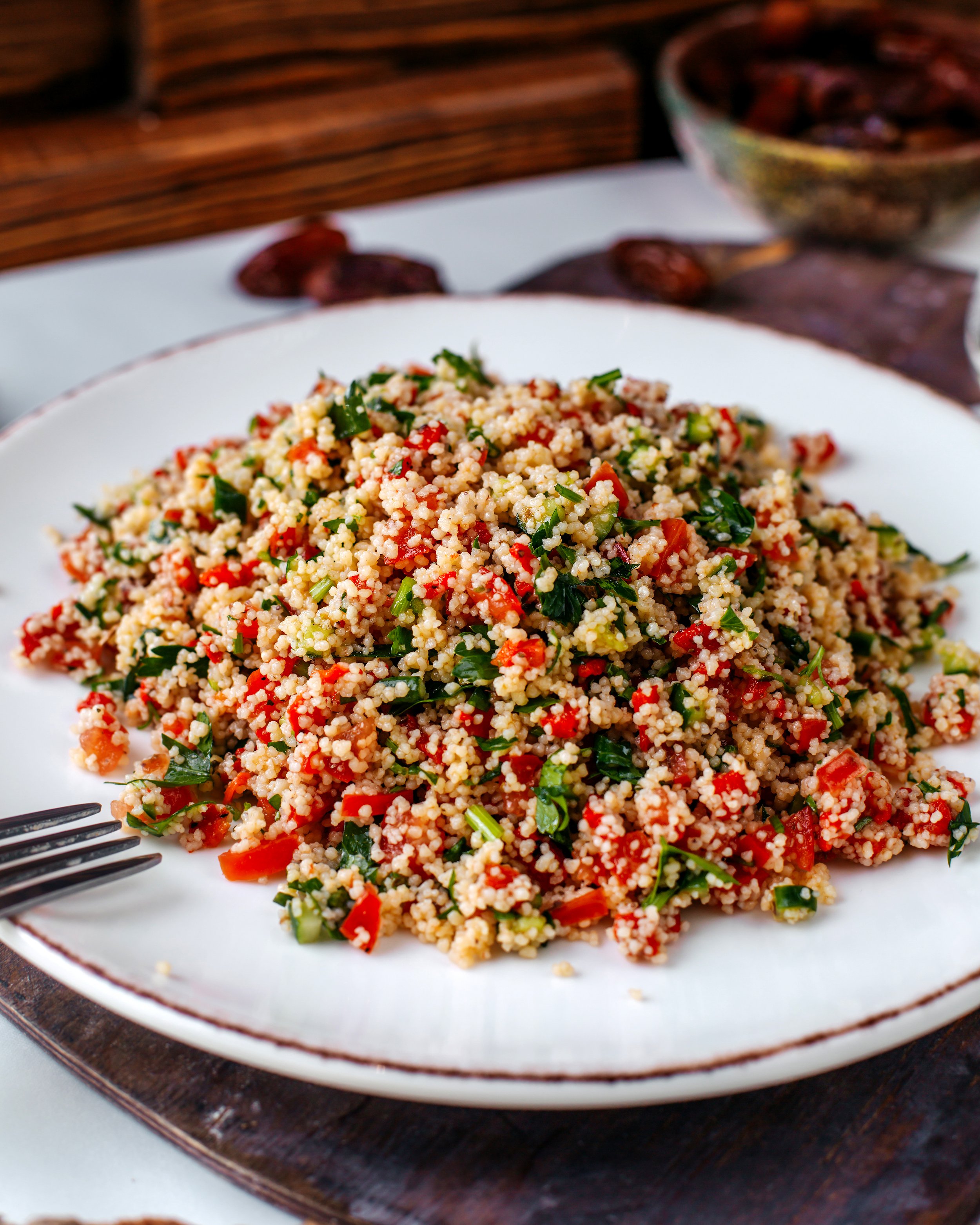 Close-up of a plate of couscous salad with chopped vegetables and herbs on a wooden serving platter.